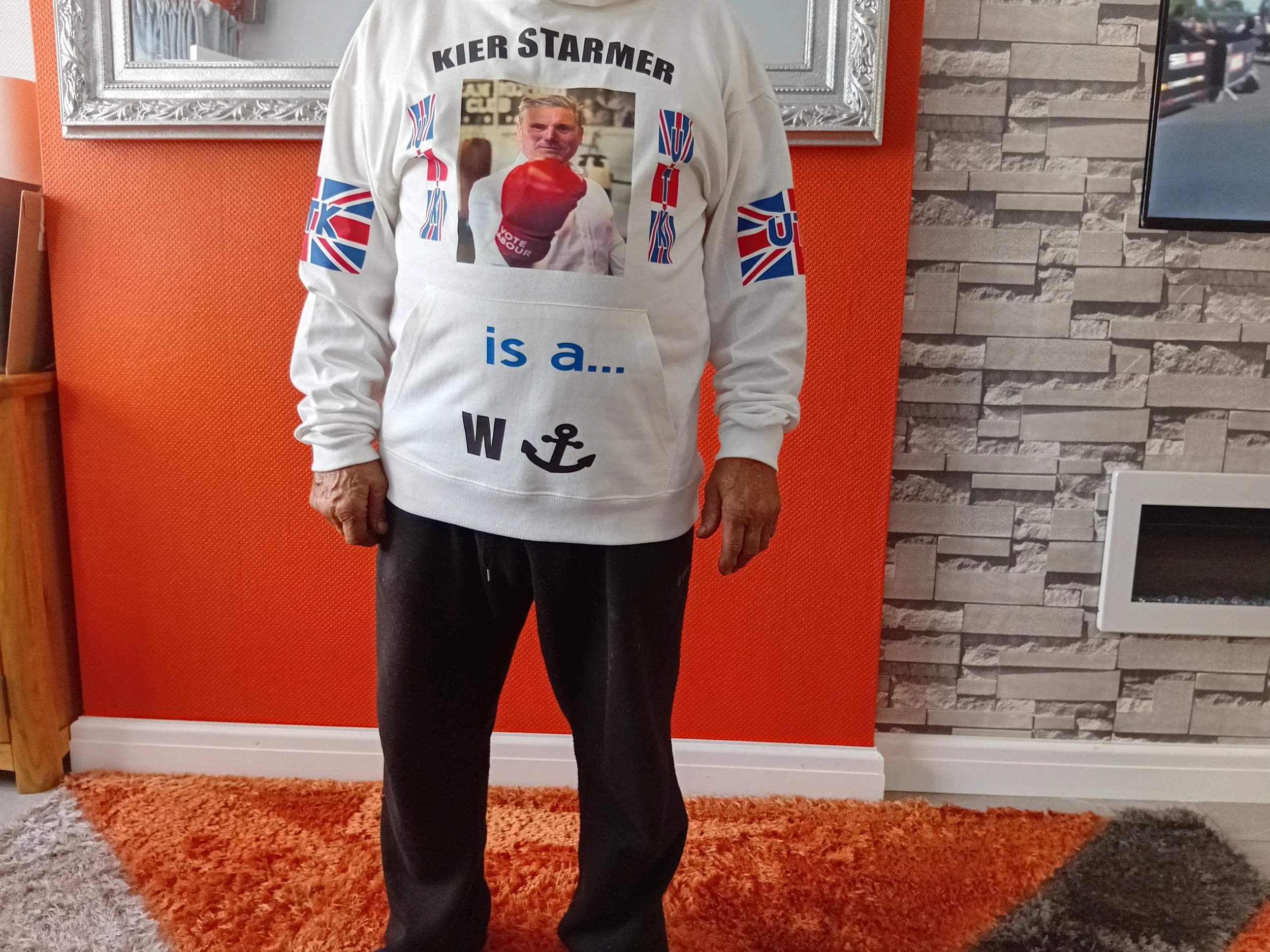Person wearing a hoodie with a photo of another person holding a boxing glove, surrounded by Union Jack flags, and the text 'Kier Starmer is a...' with an anchor symbol.