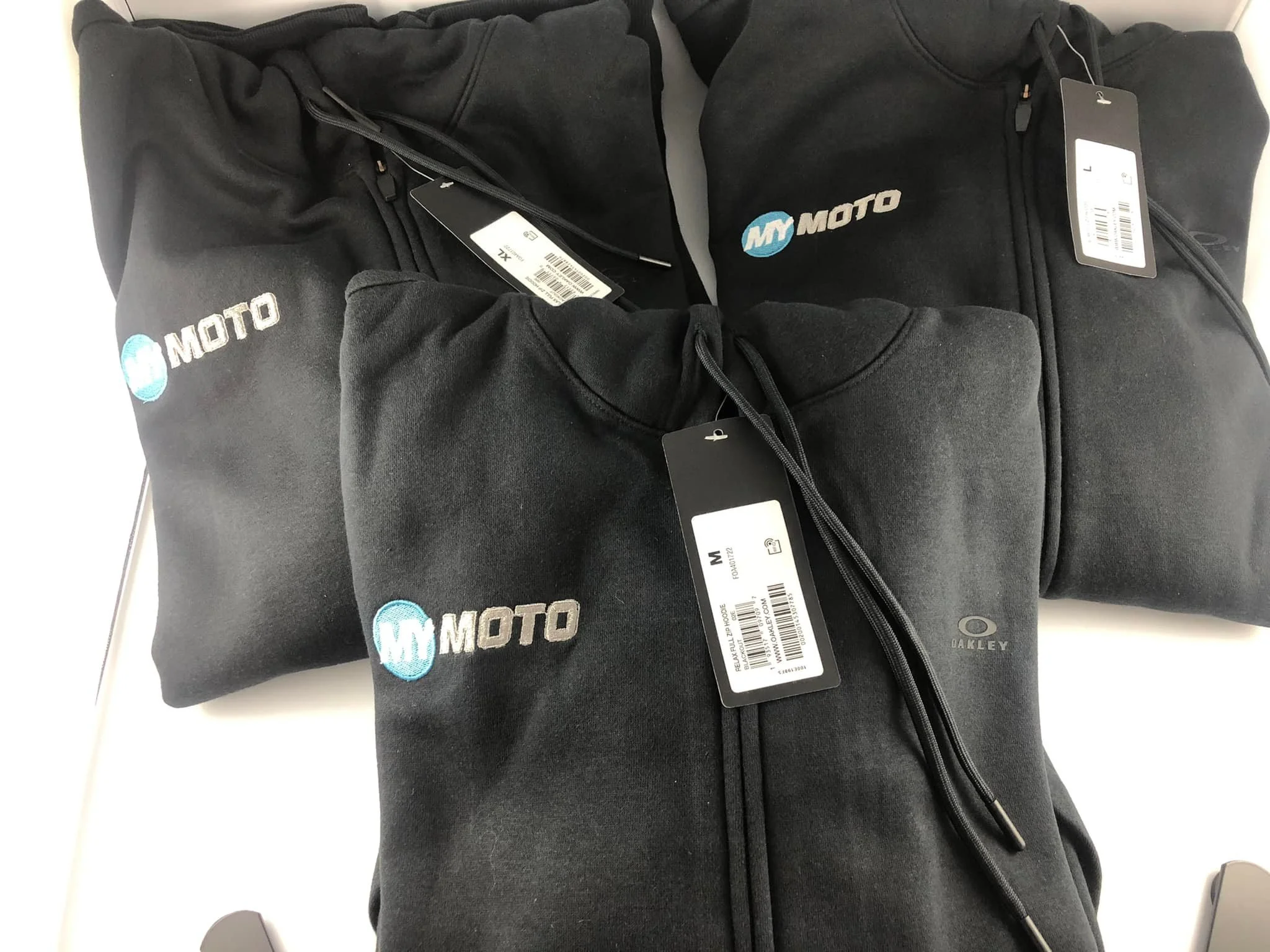 Three black hoodies with My Moto logo on a white surface, each with a price tag attached.