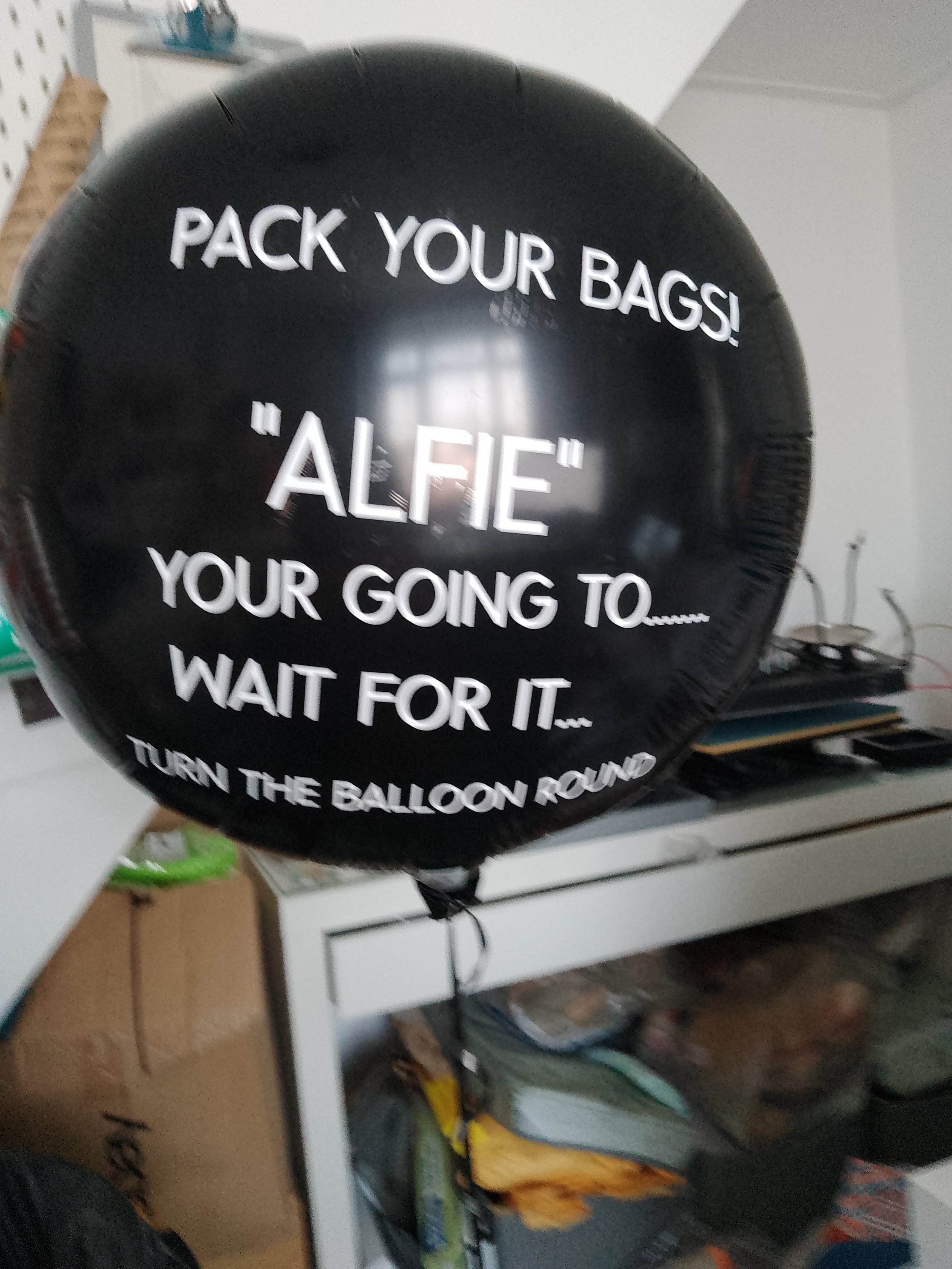 A black balloon with white text that reads: "Pack your bags! 'Alfie' your going to... wait for it... turn the balloon round."
