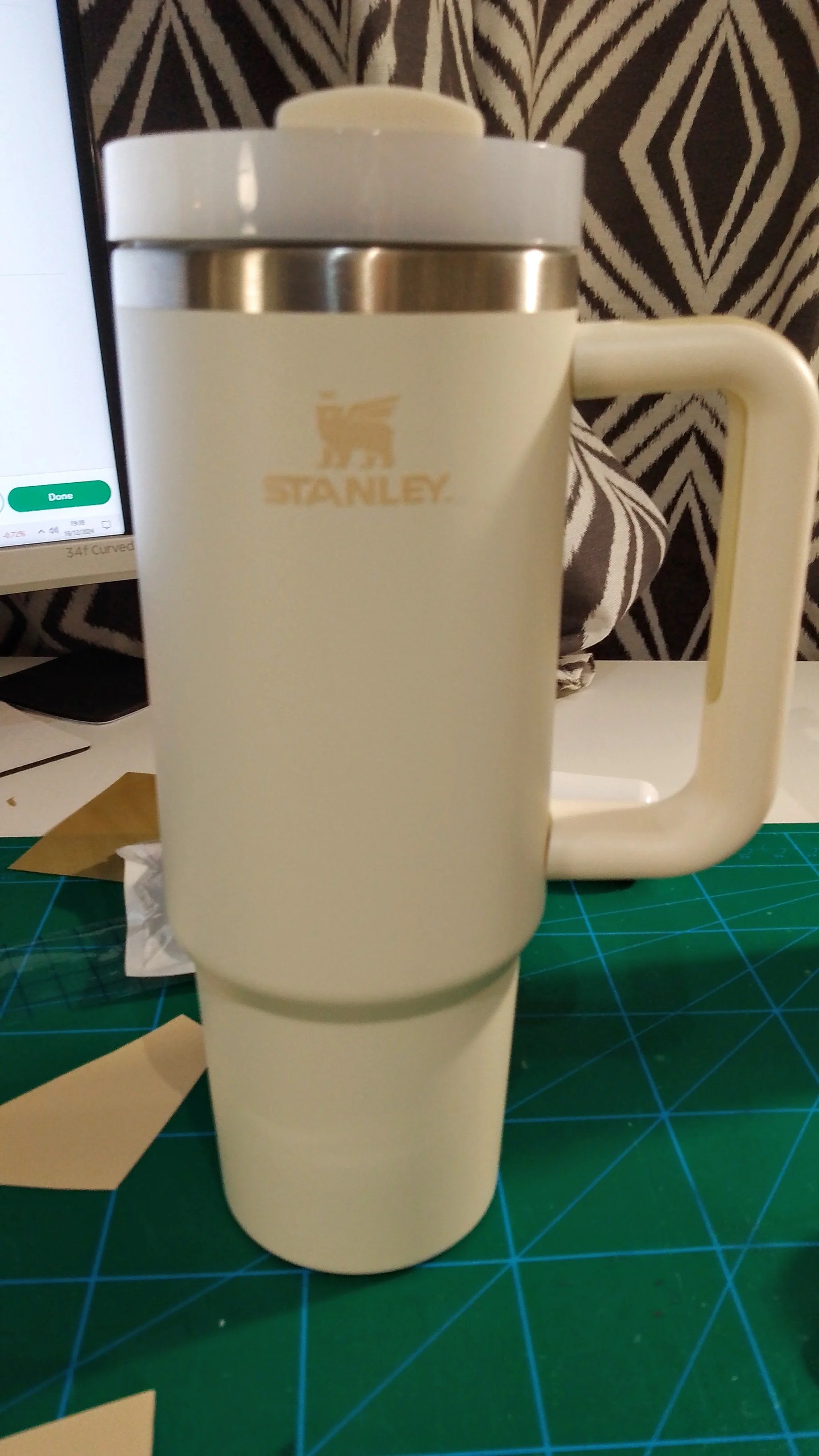 Cream-colored Stanley travel mug with a handle, placed on a green cutting mat, with a zebra pattern fabric in the background.