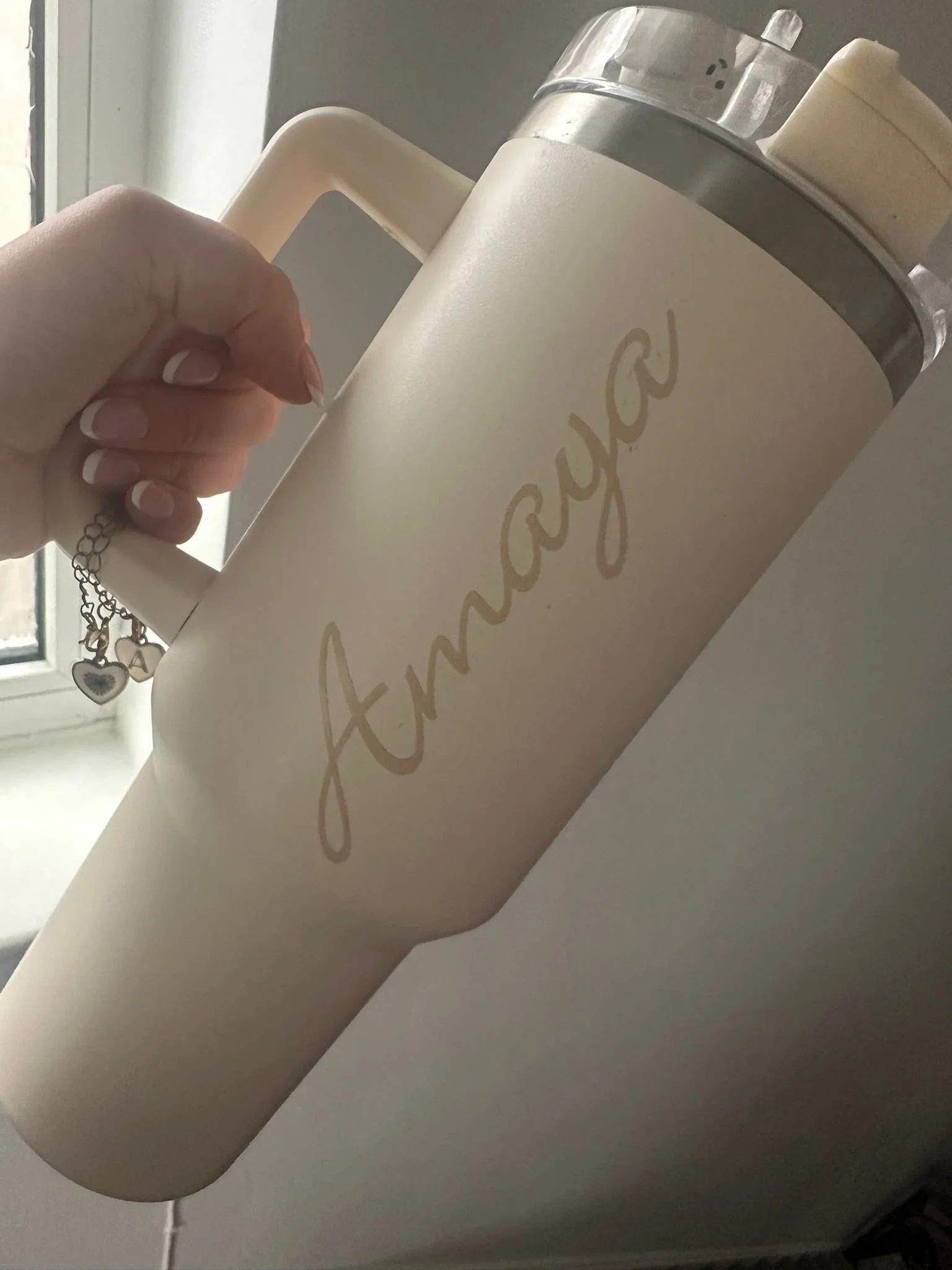 A beige insulated tumbler with the word 'anyday' written on it, held by a hand with French manicure, near a window.