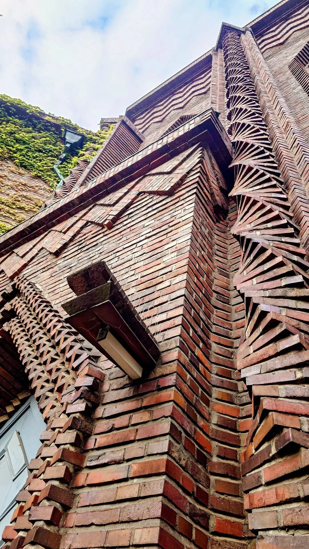Close-up view of a brick building with geometric brick patterns, stairs, and a window seen from below during daytime.