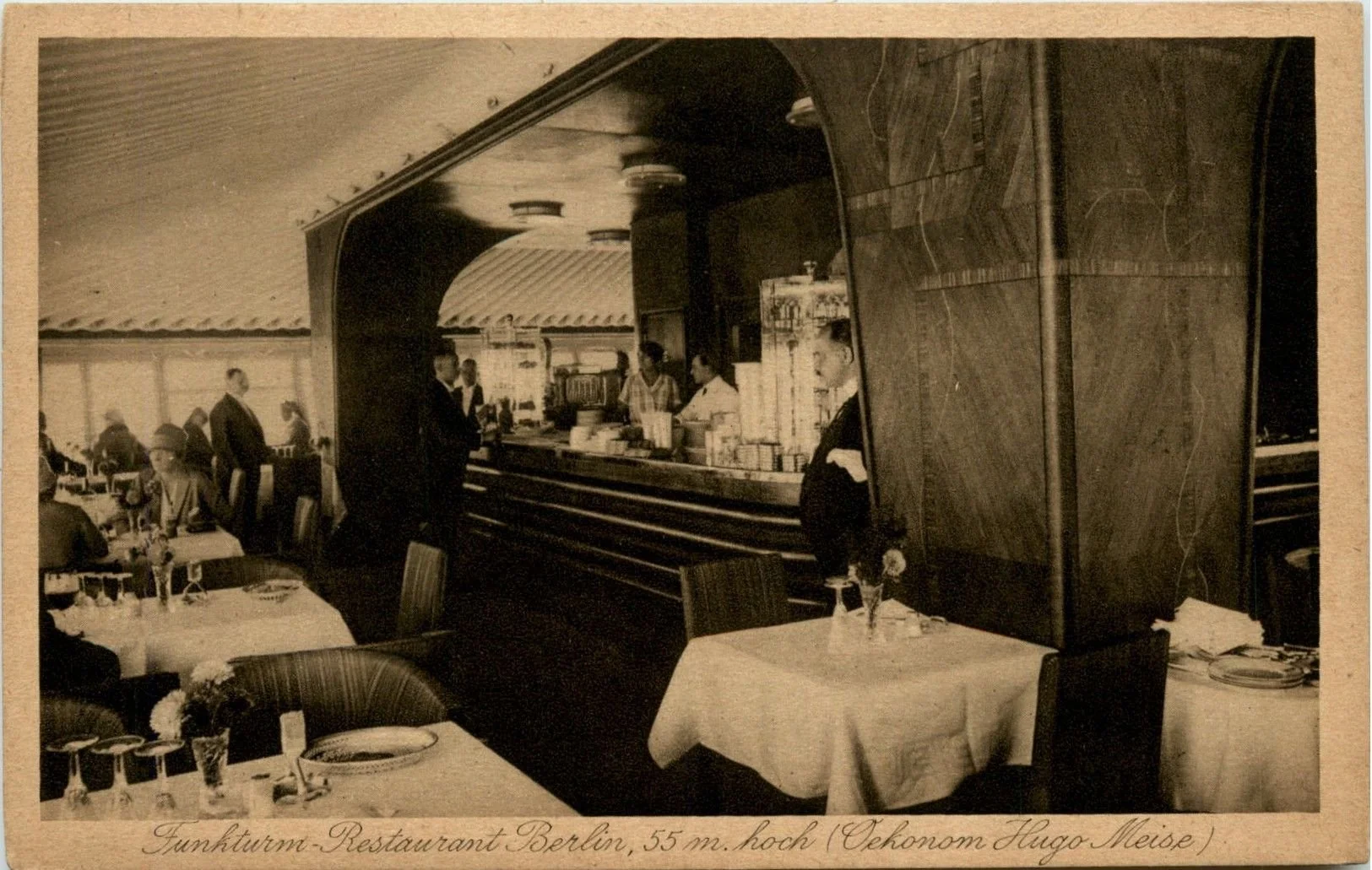 Interior of a restaurant with tables set for dining, including wine glasses and plates, and a bar with staff and customers in the background. The caption notes it is a Tunkturm restaurant in Berlin, 55 meters high, with reference to Okonom Hugo Meise.