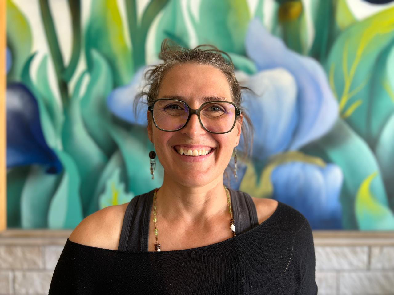 Smiling woman with glasses standing in front of colorful abstract mural
