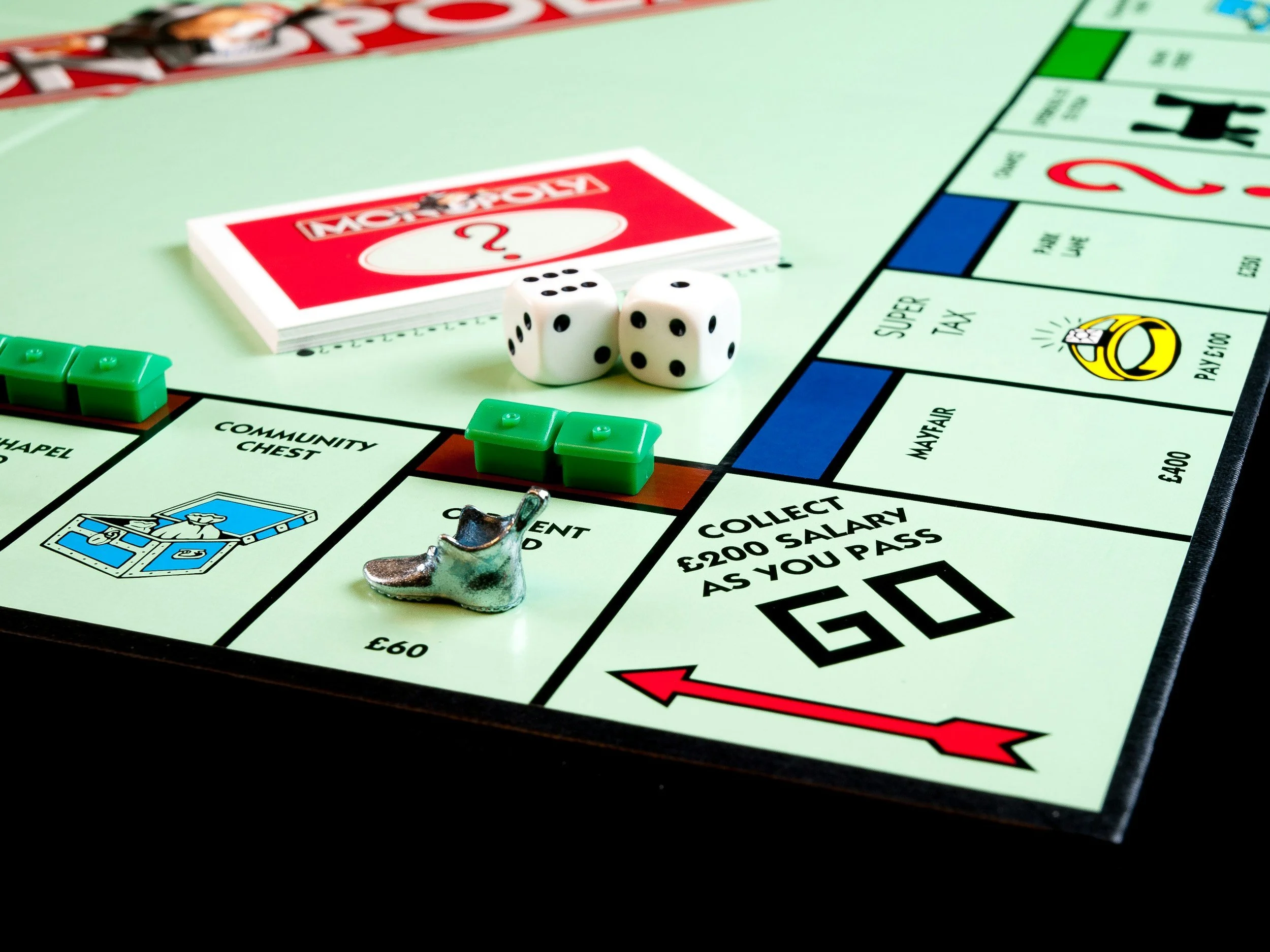 Close-up of a Monopoly game board with green houses, two white dice, a Community Chest card, and a silver shoe token.