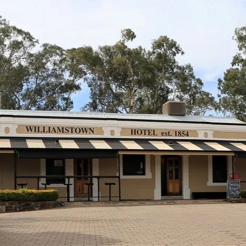 Front view of Williamstown Hotel, established in 1854, with a sidewalk, trees, and a blackboard outside.