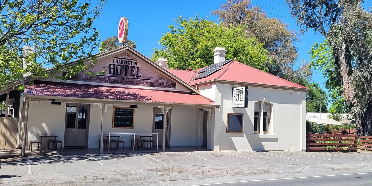 Front view of the Charleston Hotel, a white building with a pink roof, a porch with tables, and signs indicating its name.