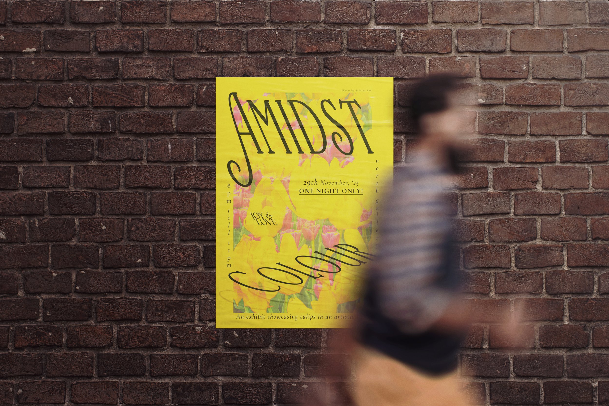 A person walking past a yellow poster on a brick wall. The poster advertises an exhibit titled 'SyMIDSToR' featuring tulips, with event details including date, time, and theme of 'Joy & Love'.