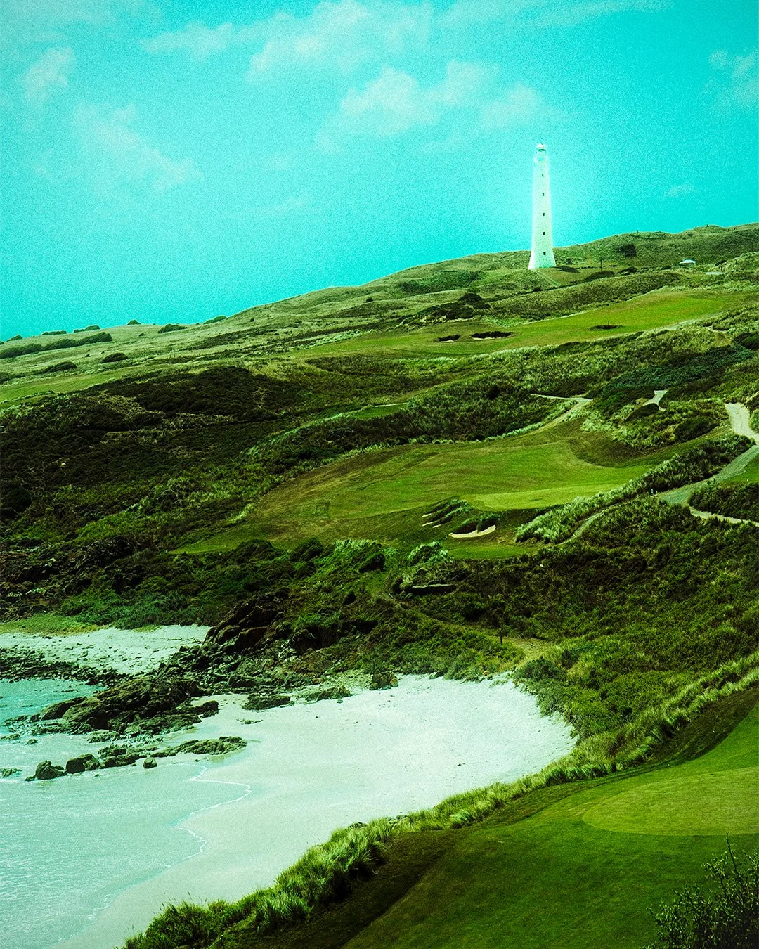 Scenic coastal landscape with a lighthouse on a hill, green fields, winding paths, and a beach with rocks and waves.