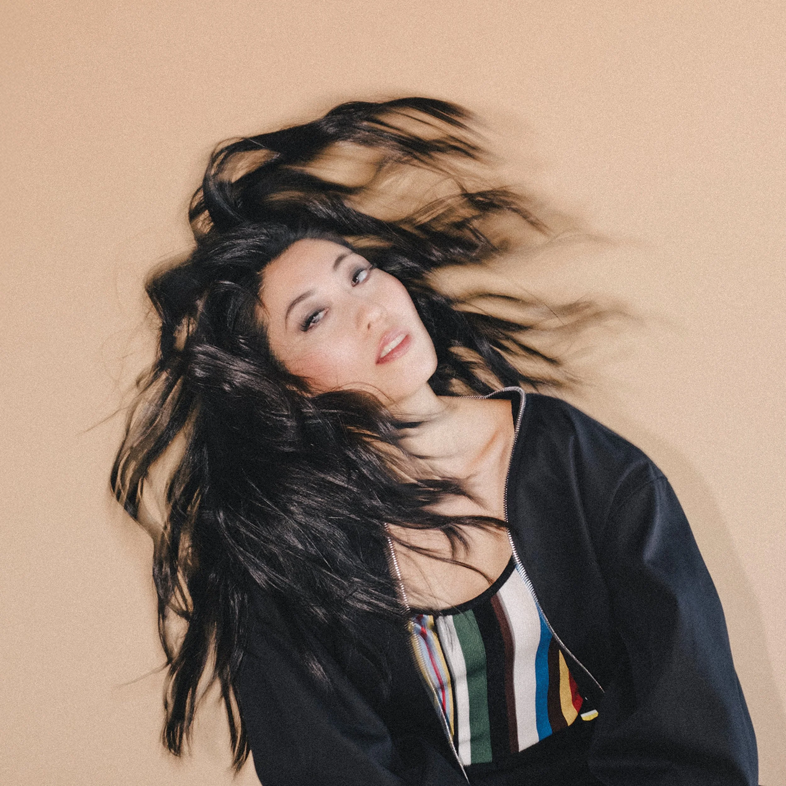 Wanting Qu flipping her hair, looking up and smiling, wearing a striped shirt with various colors.