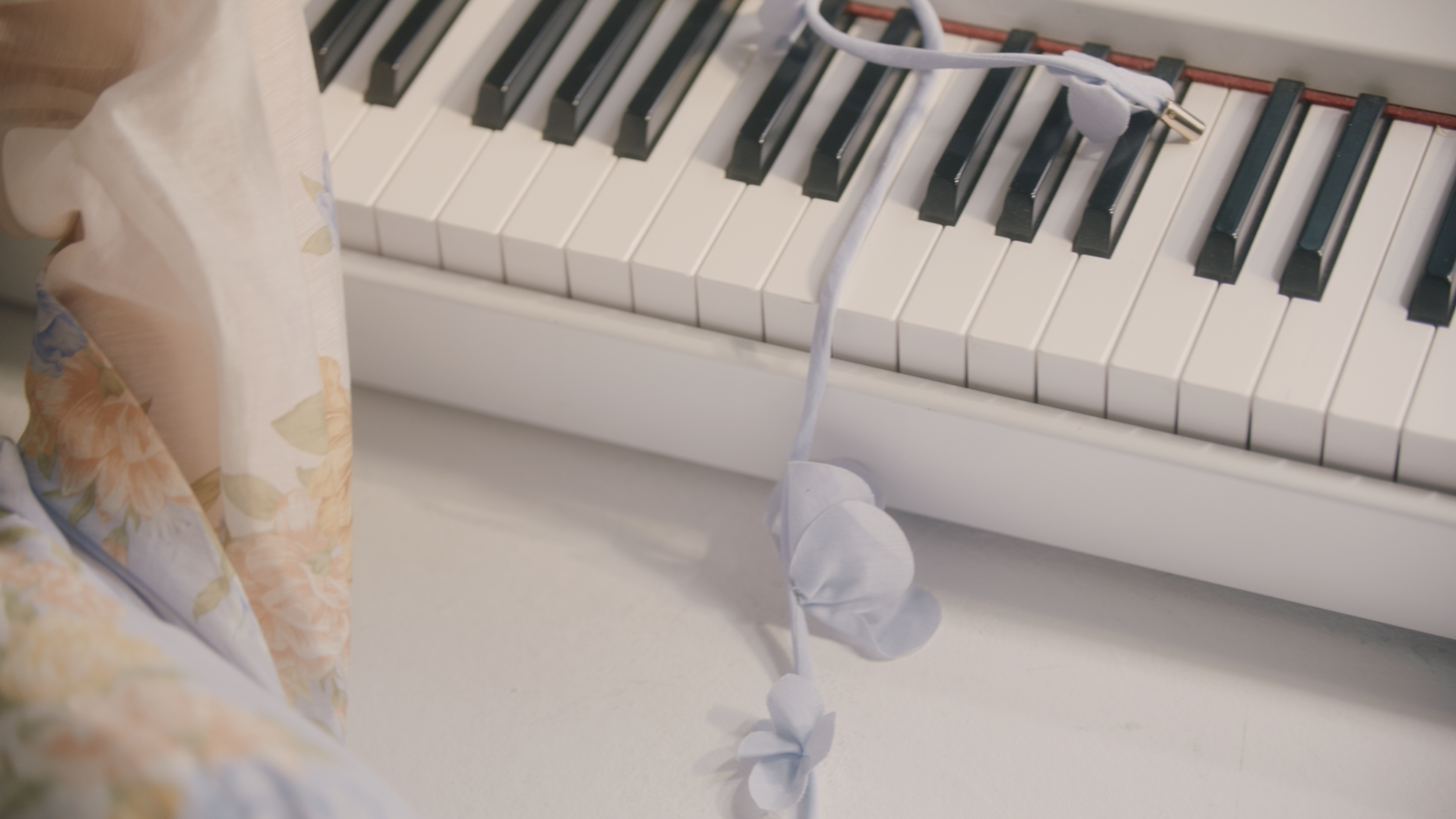 Close-up of a pink and white digital piano with a white braided cord on top, and a floral-patterned skirt or dress in the foreground.