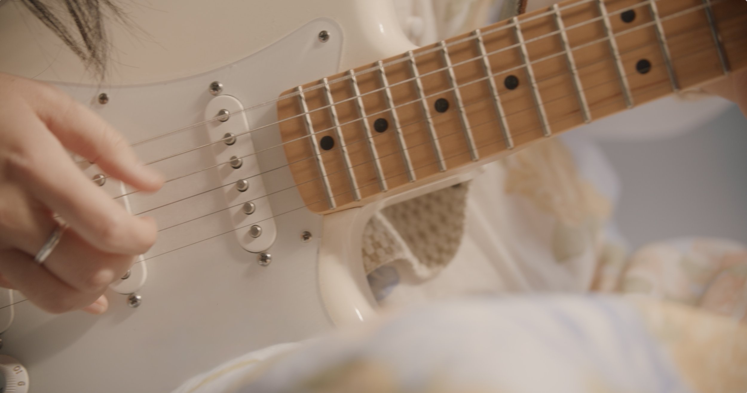 Close-up of Wanting Qu playing a white electric guitar, with herleft hand on the fretboard.