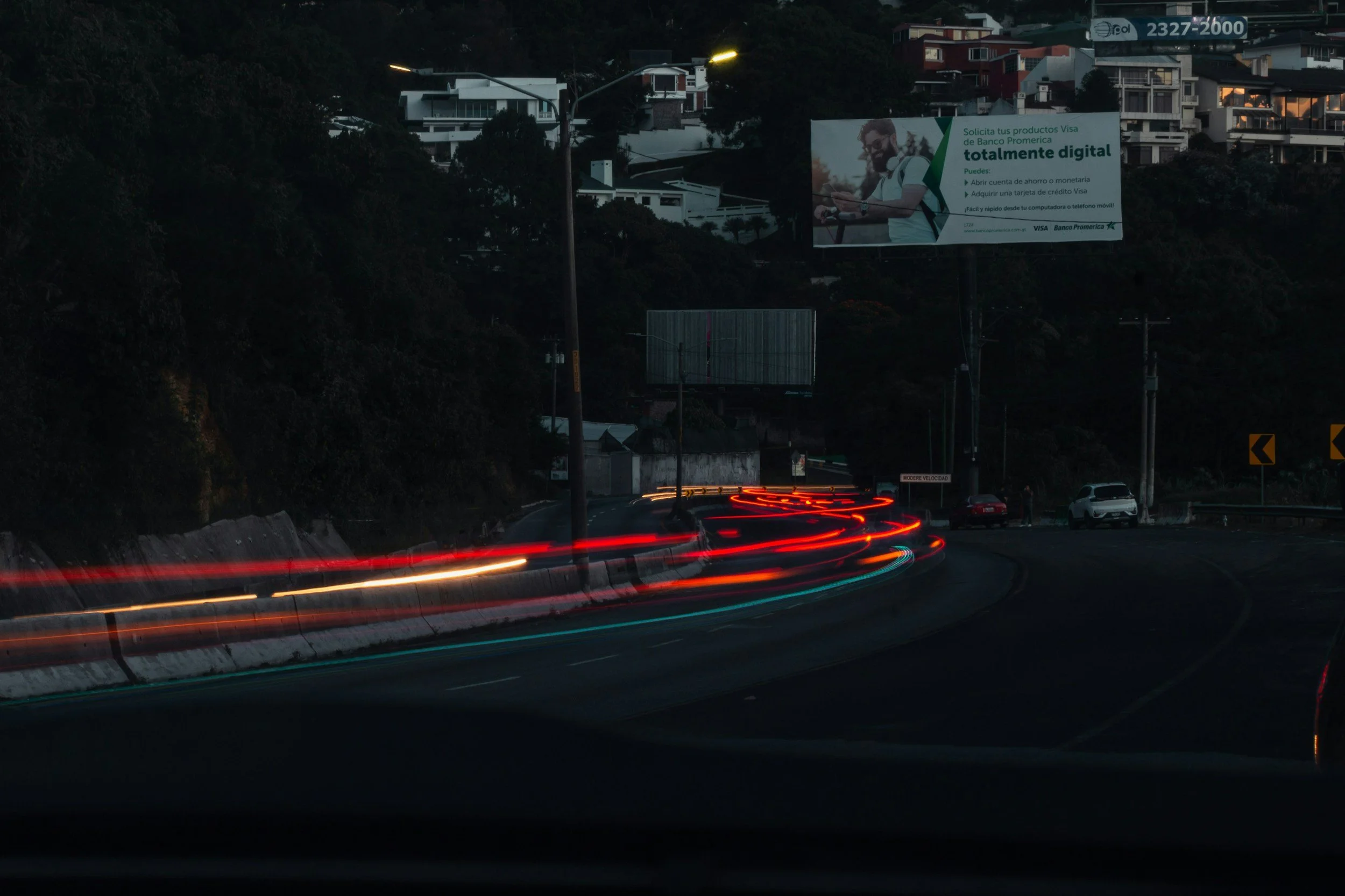 A mountainous landscape with snow-capped peaks in the background, rolling green and brown hills in the foreground, and a modern building nestled on the hillside.