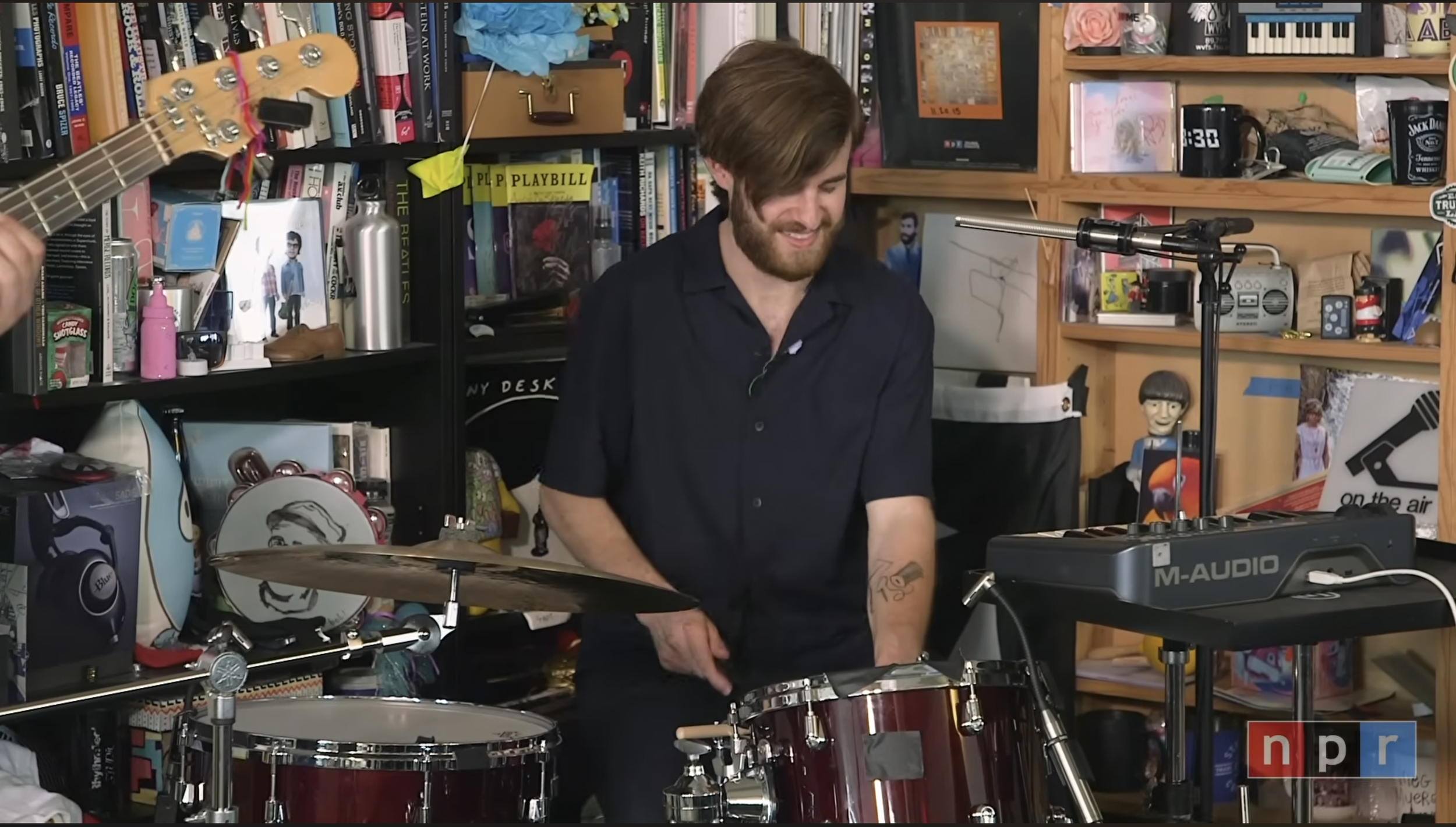 A man with a beard and long brown hair playing a large drum set with a keyboard and other musical equipment at the NPR Music Tiny Desk in Washington, D.C.