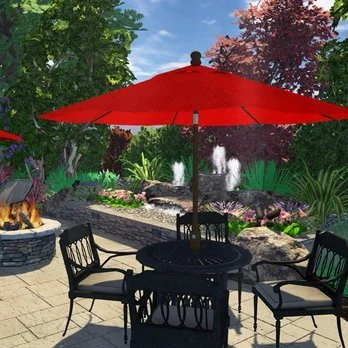 Patio with black table and chairs under a red umbrella, fountain, flowers, trees, and rocks in the background.