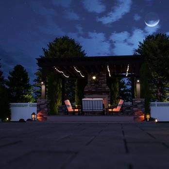 An outdoor patio area at night under a crescent moon, featuring a pergola with string lights, two pink chairs, a table, and some greenery.
