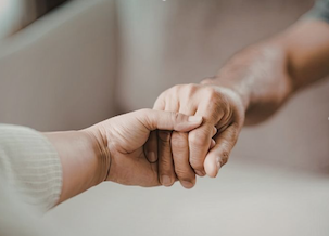 White hand and brown hand holding each other, representing comfort in grief support group