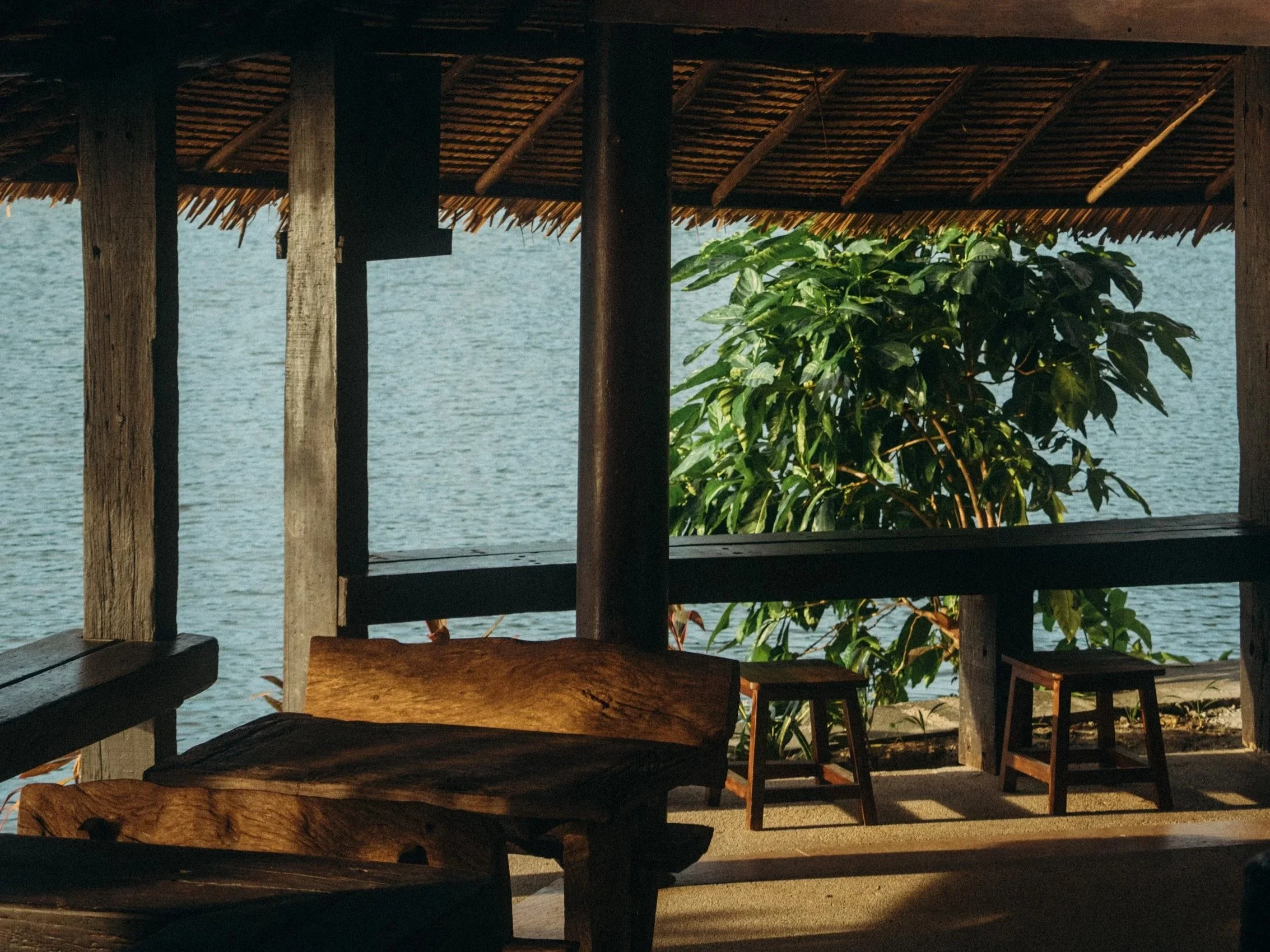 Interior of The Lakehouse. A rustic wooden Bali charm indoor seating area surrounded by the lake. with a wooden bench and with chairs