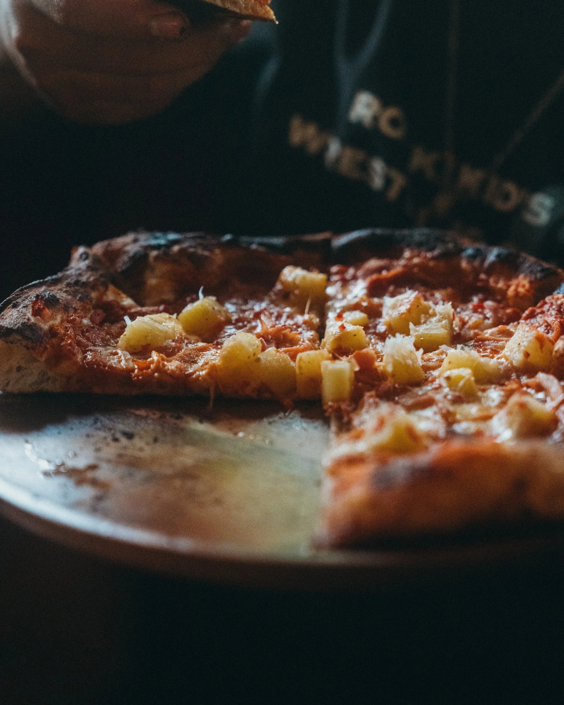 A slice of hawaii pizza on a wooden tray, a few slices are taken or already eaten in The Lakehouse
