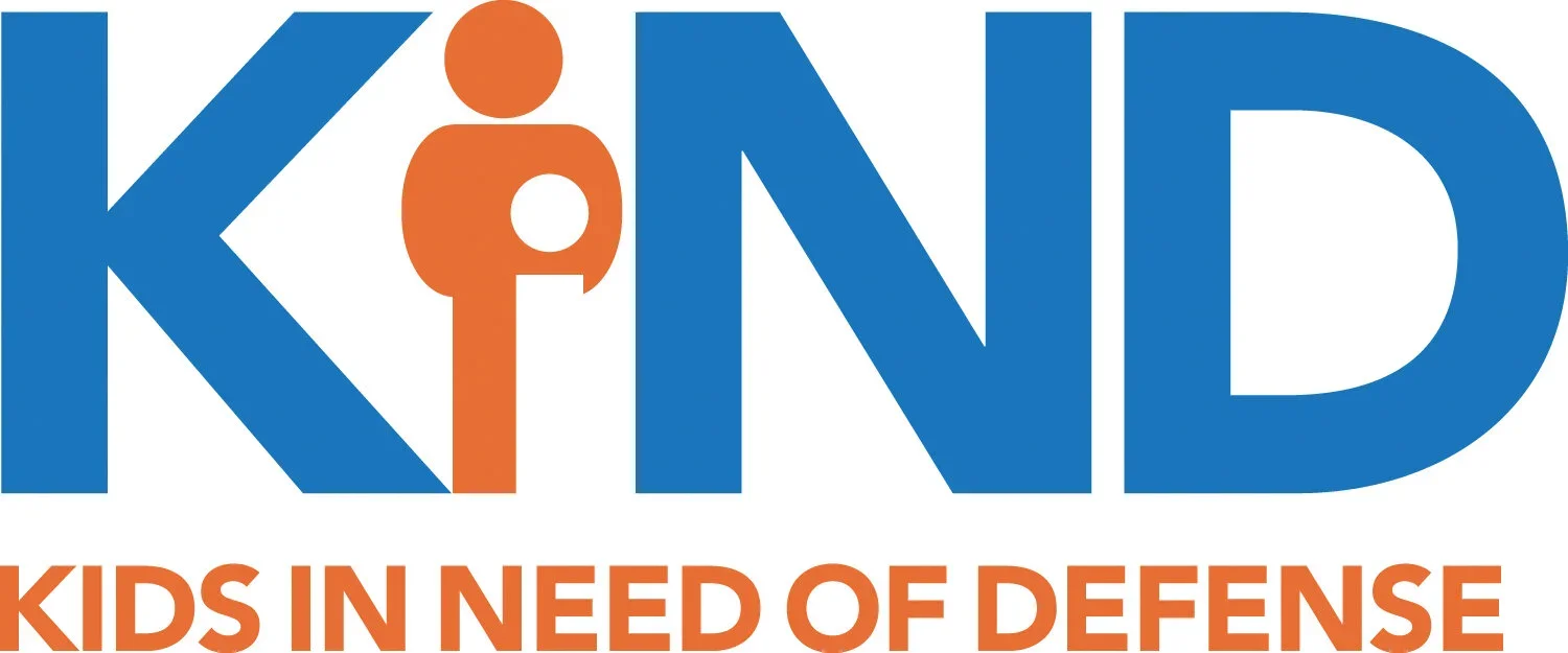 Logo for Kids in Need of Defense (KIND), featuring the word 'KIND' in blue with an orange stylized person in the middle, and the tagline 'Kids in Need of Defense' below in orange.