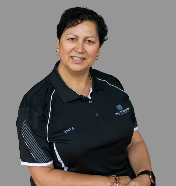 A woman with short dark hair, wearing a black polo shirt with white accents and a logo, standing against a gray background.