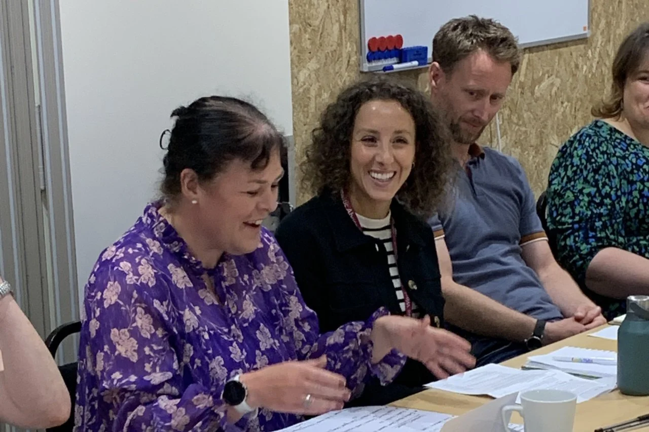 Group of four people sitting at a table during a meeting, smiling and engaging with documents.