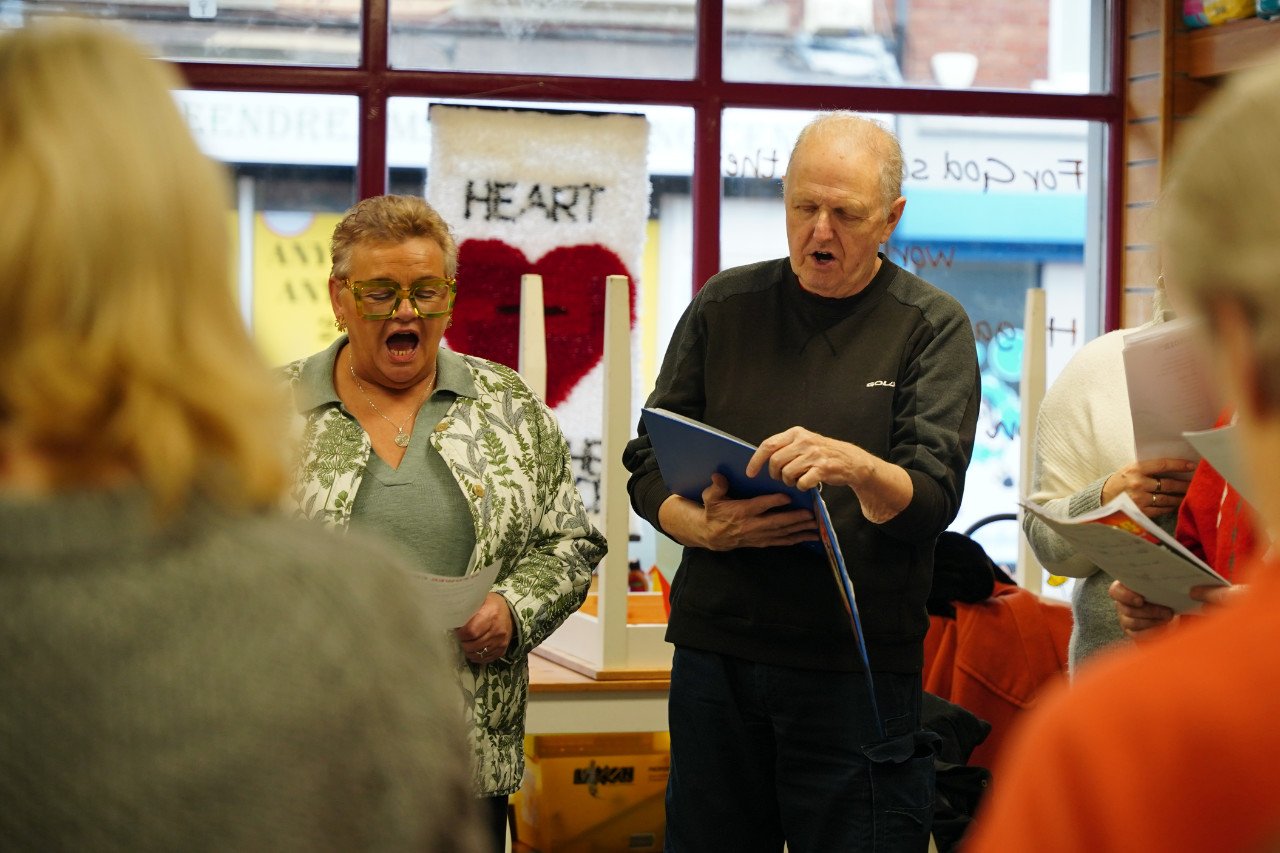 People singing together indoors with a mural of a heart on the wall behind them.