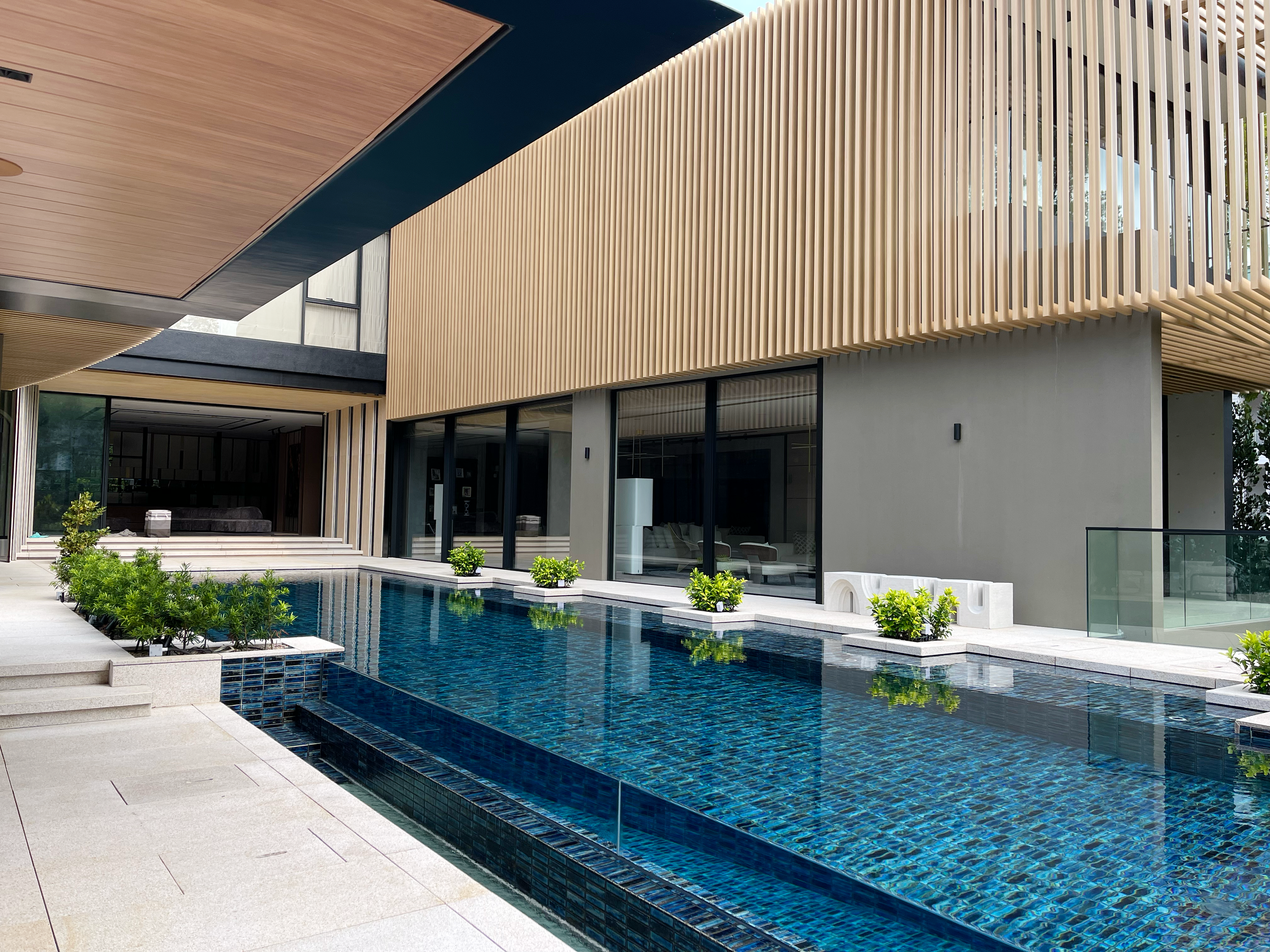 Modern house with a swimming pool surrounded by potted plants and a deck, featuring large glass windows and wooden slats for exterior decor.