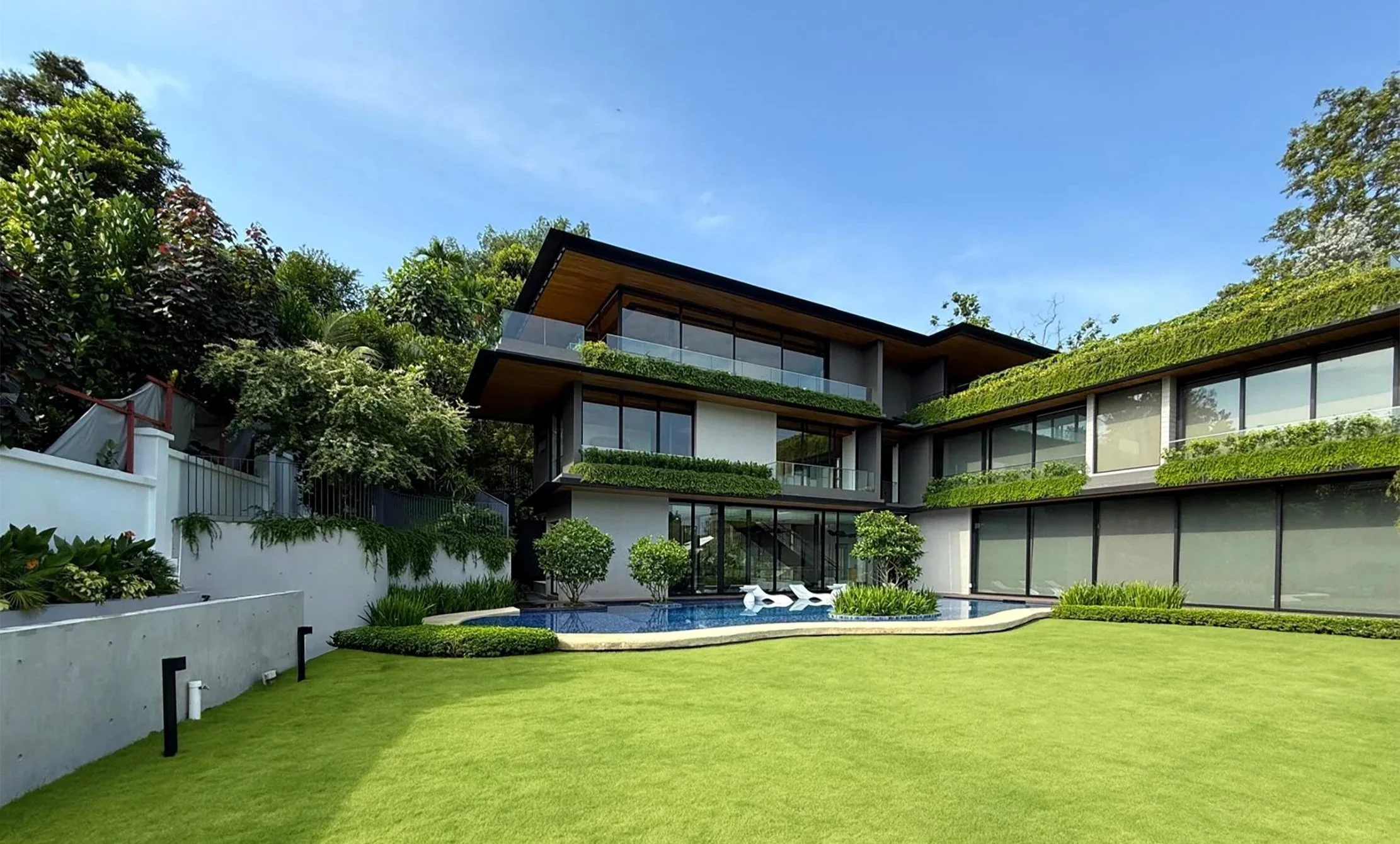 Modern multi-story house with large glass windows, surrounded by a landscaped lawn and greenery, featuring a reflecting pool with white swan sculptures.
