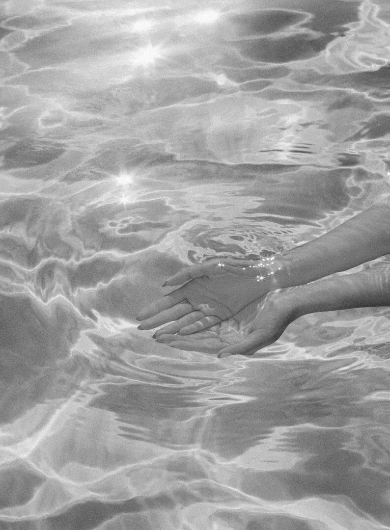 Two hands gently holding each other under water in a swimming pool with sunlight reflections.