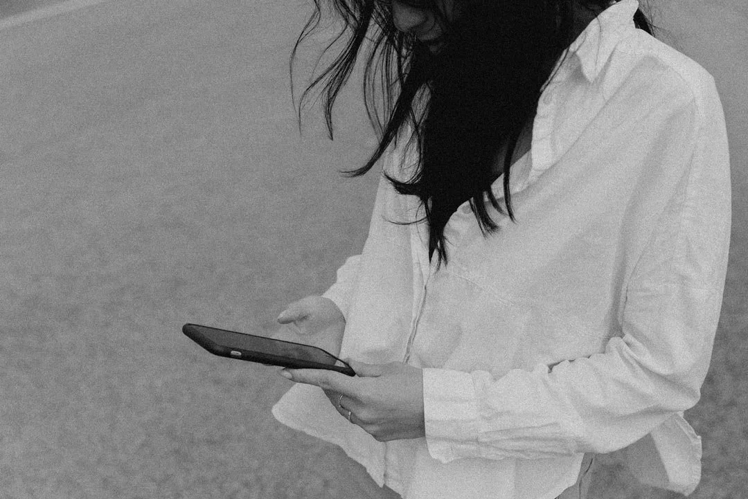 A woman in a white shirt looking down at her smartphone.