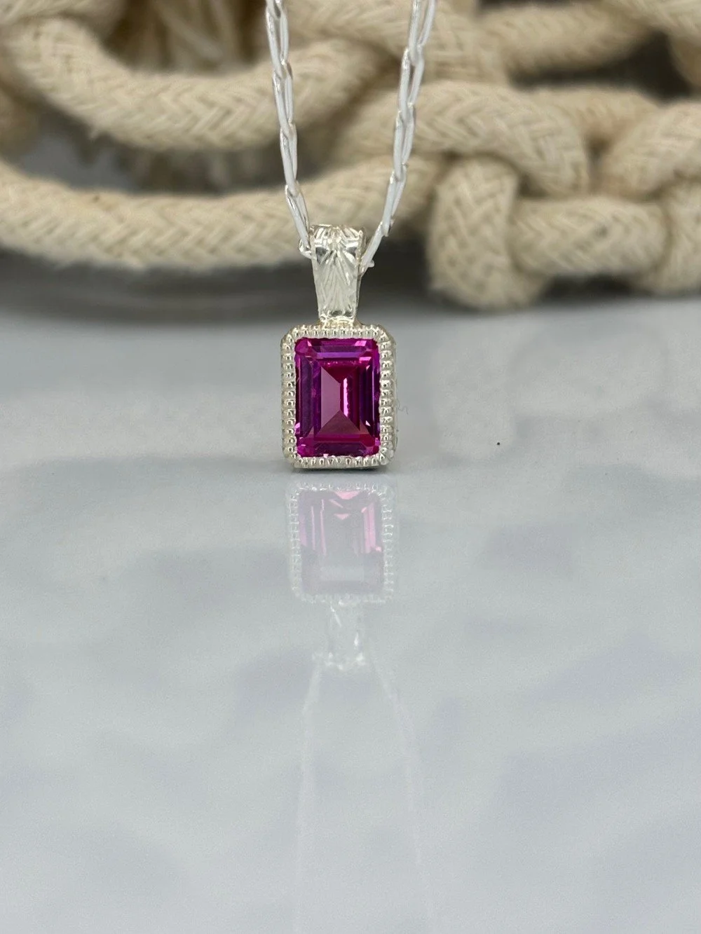 A pink emerald cut gemstone in a silver setting with milgrain and hand-engraving