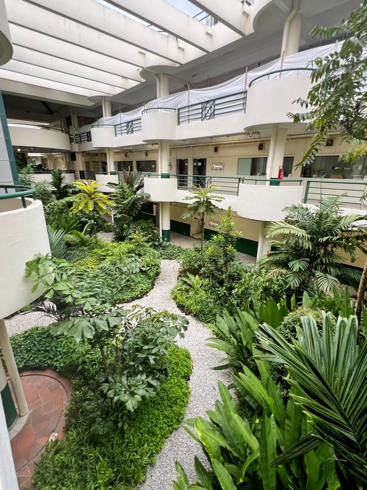 Indoor courtyard with lush green plants and gravel pathway in a multi-level building with white walls and ceilings.