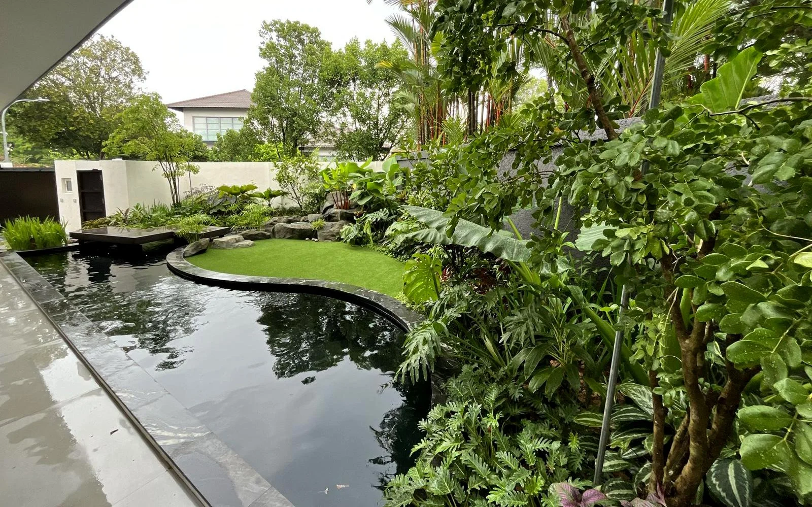 Modern backyard garden with a water feature, greenery, and a small grassy area.