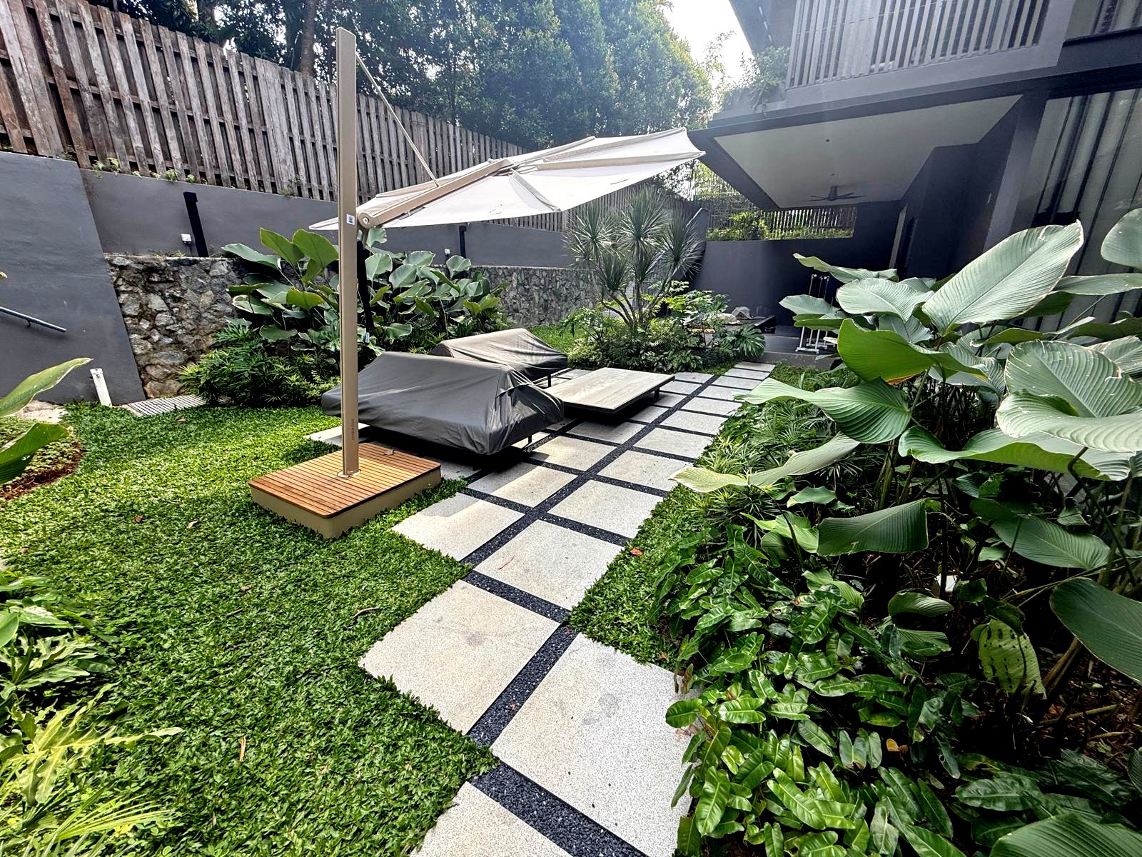 Modern backyard with a pathway, green plants, and outdoor seating under an umbrella.