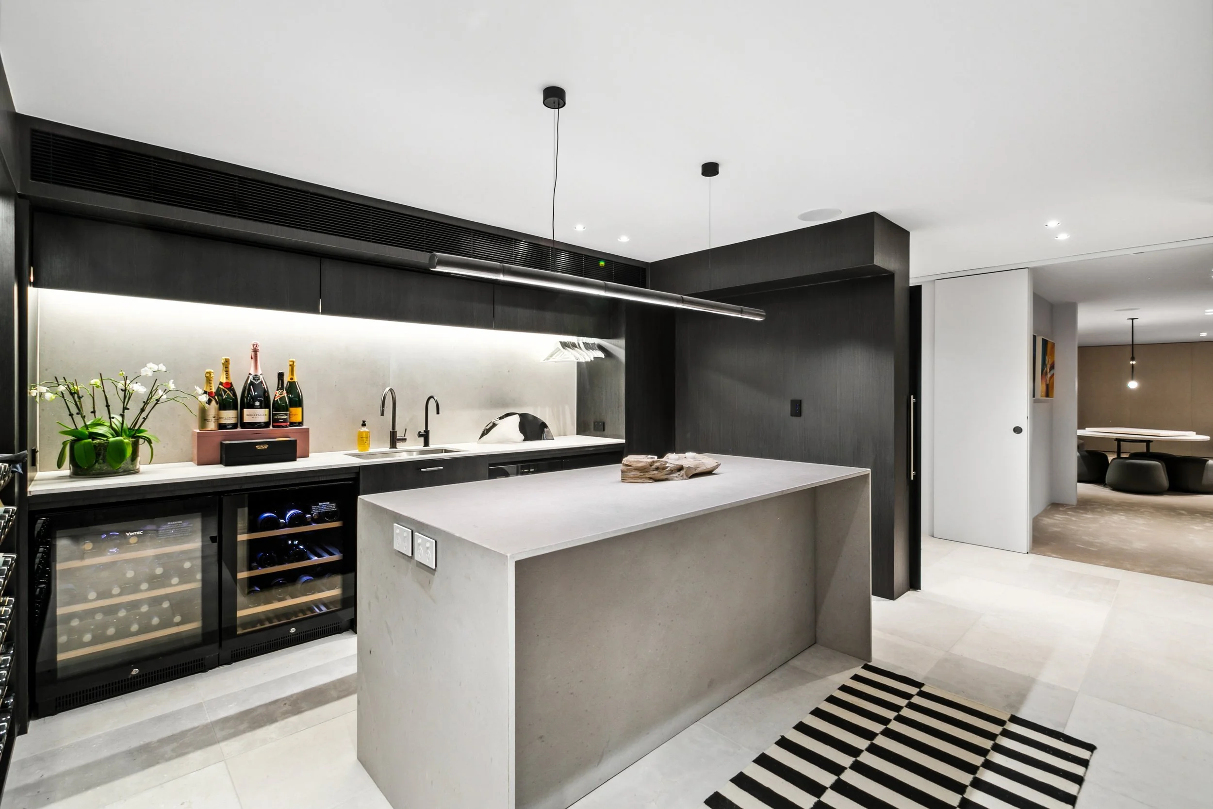 Modern kitchen with black and white color scheme, wine cooler, potted plant, bottles of champagne, and a dog on the countertop.