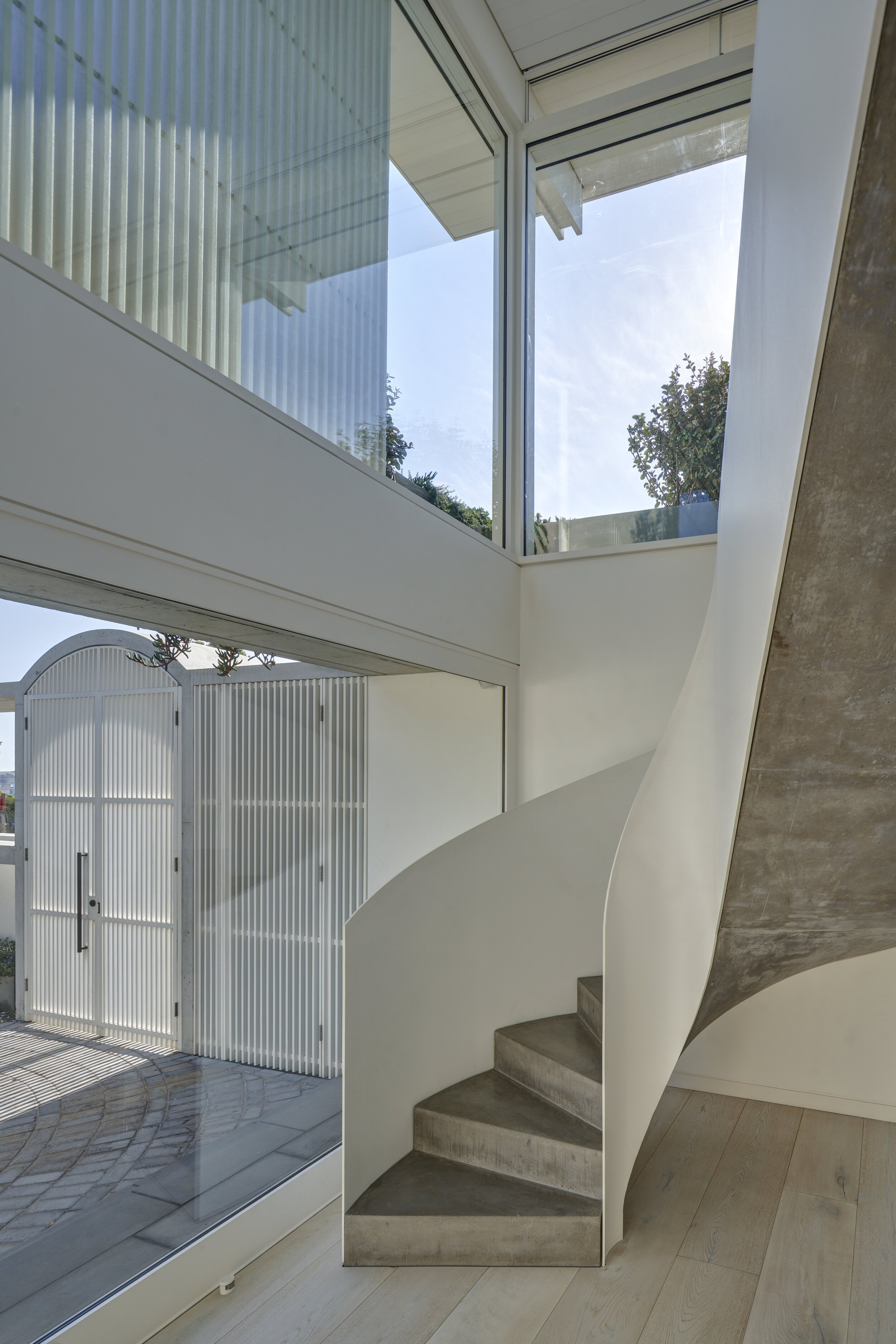 Modern interior with a concrete staircase, large glass windows, and white walls, leading to a second floor with a view of the outdoors.