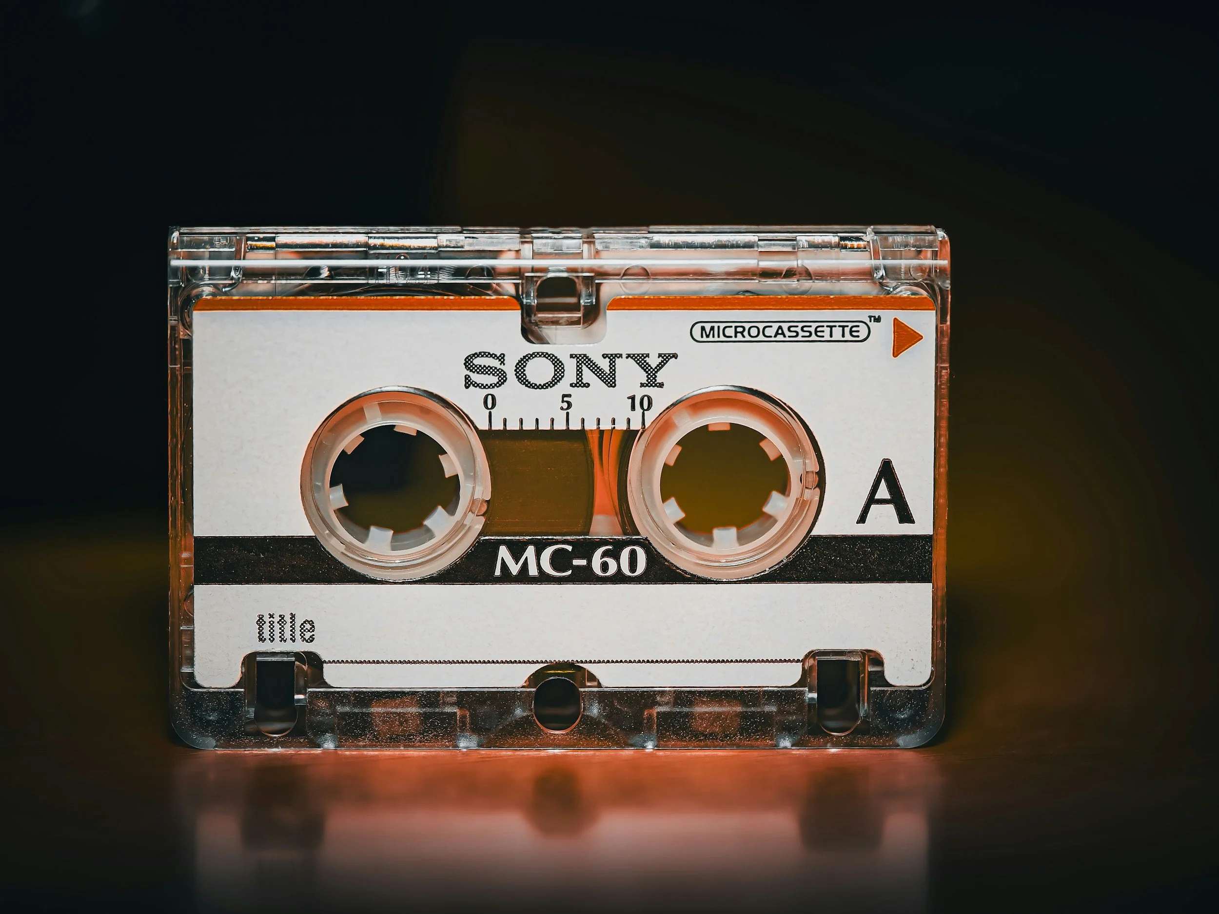 Close-up of a vintage Sony MC-60 microcassette tape with a white label and black text, placed on a reflective surface with a dark background.