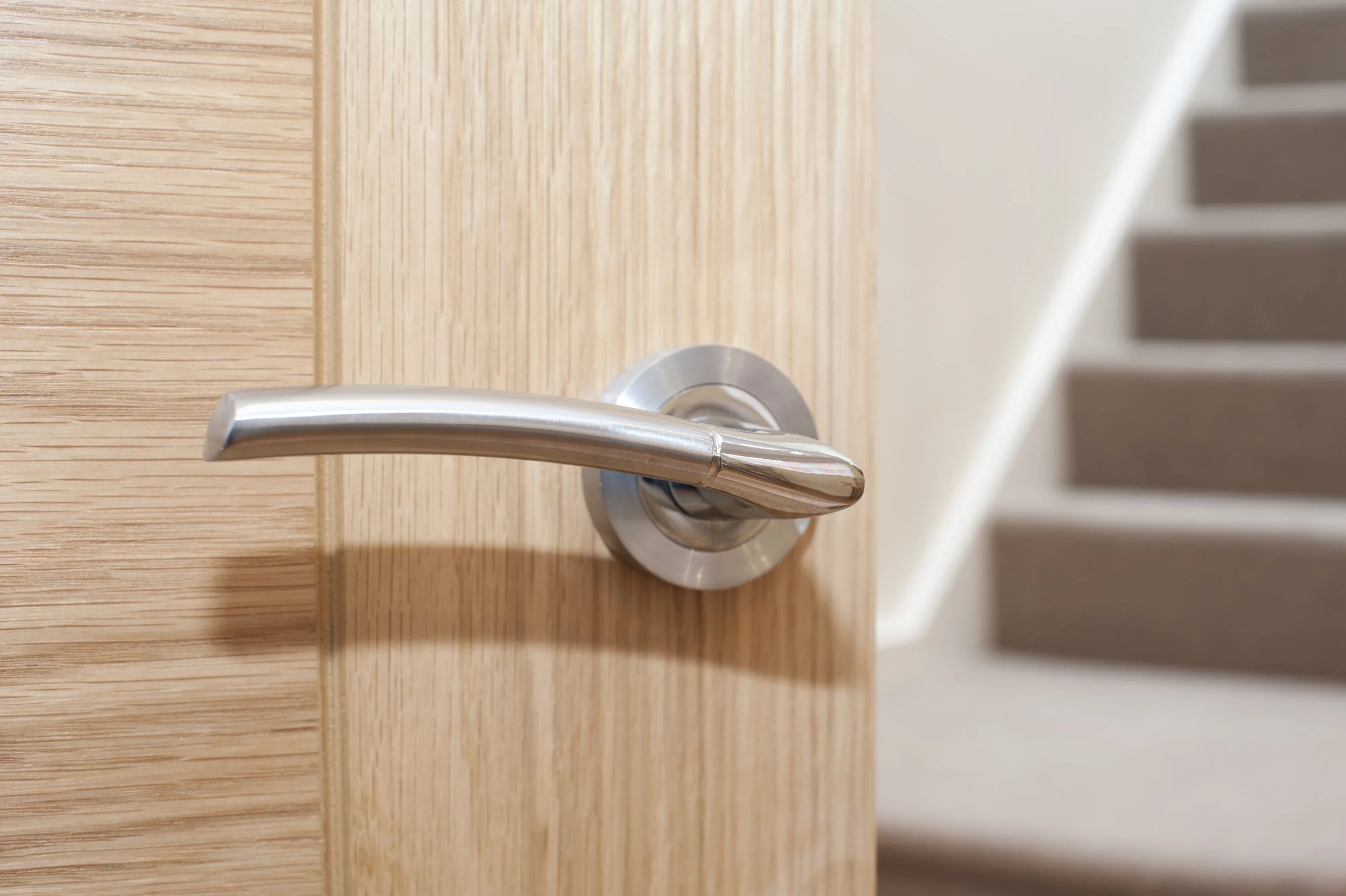 Close-up of a silver door handle on a wooden door near a staircase.