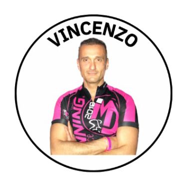 Portrait of a man in a pink and black cycling jersey with arms crossed, in front of a circular logo with the name 'Vincenzo'.