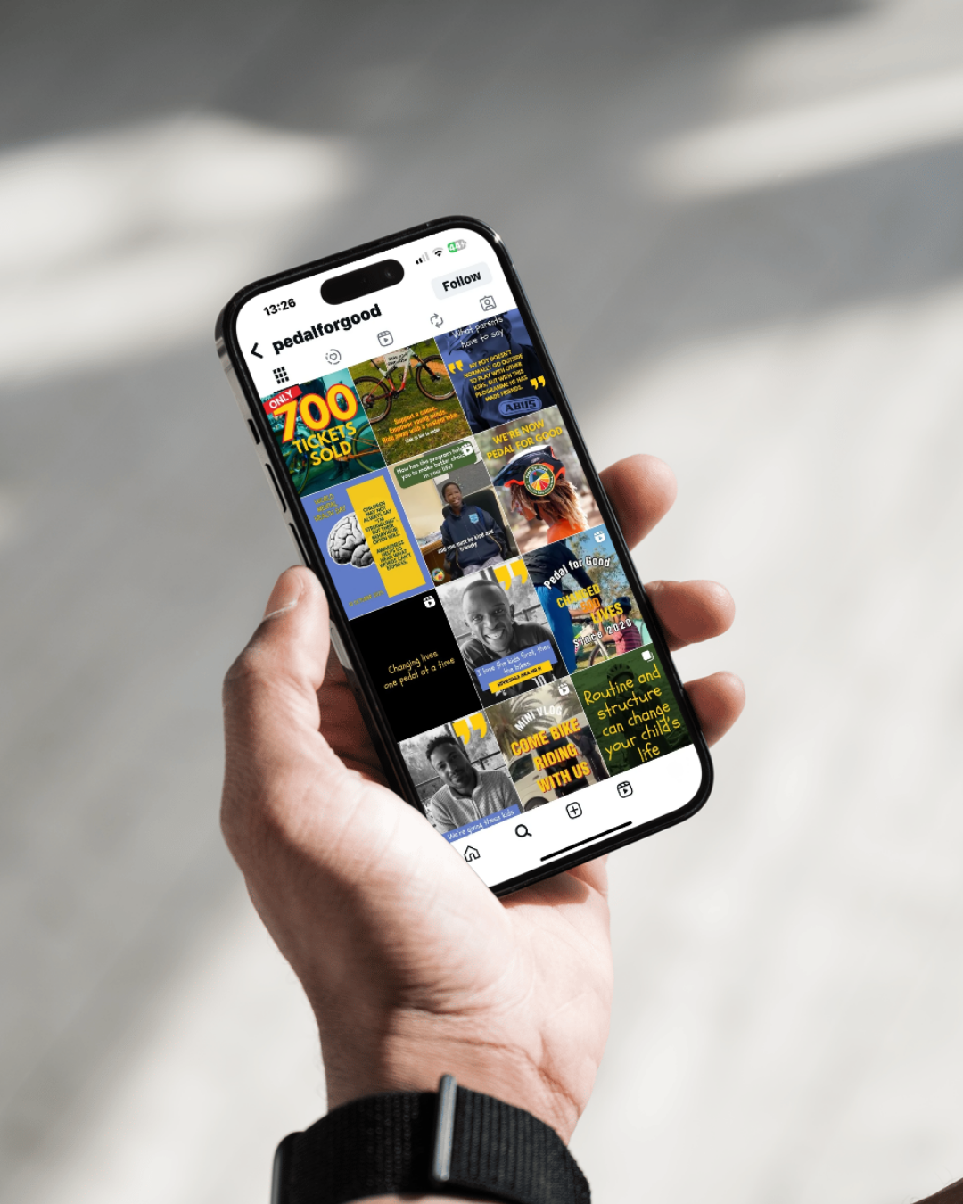 Close-up of a hand holding a smartphone displaying an Instagram profile called 'pedalforgood' with various colorful posts related to biking and community events.