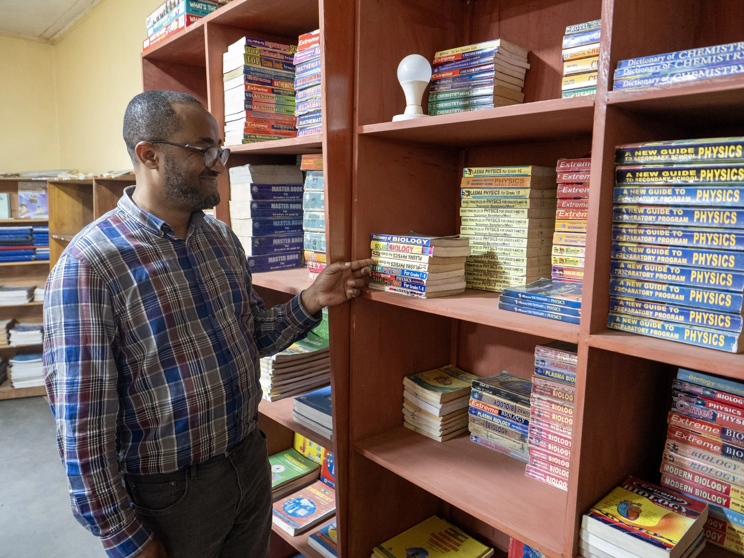 Mies seisoo kirjahyllyn edessä katsellen oppikirjoja.