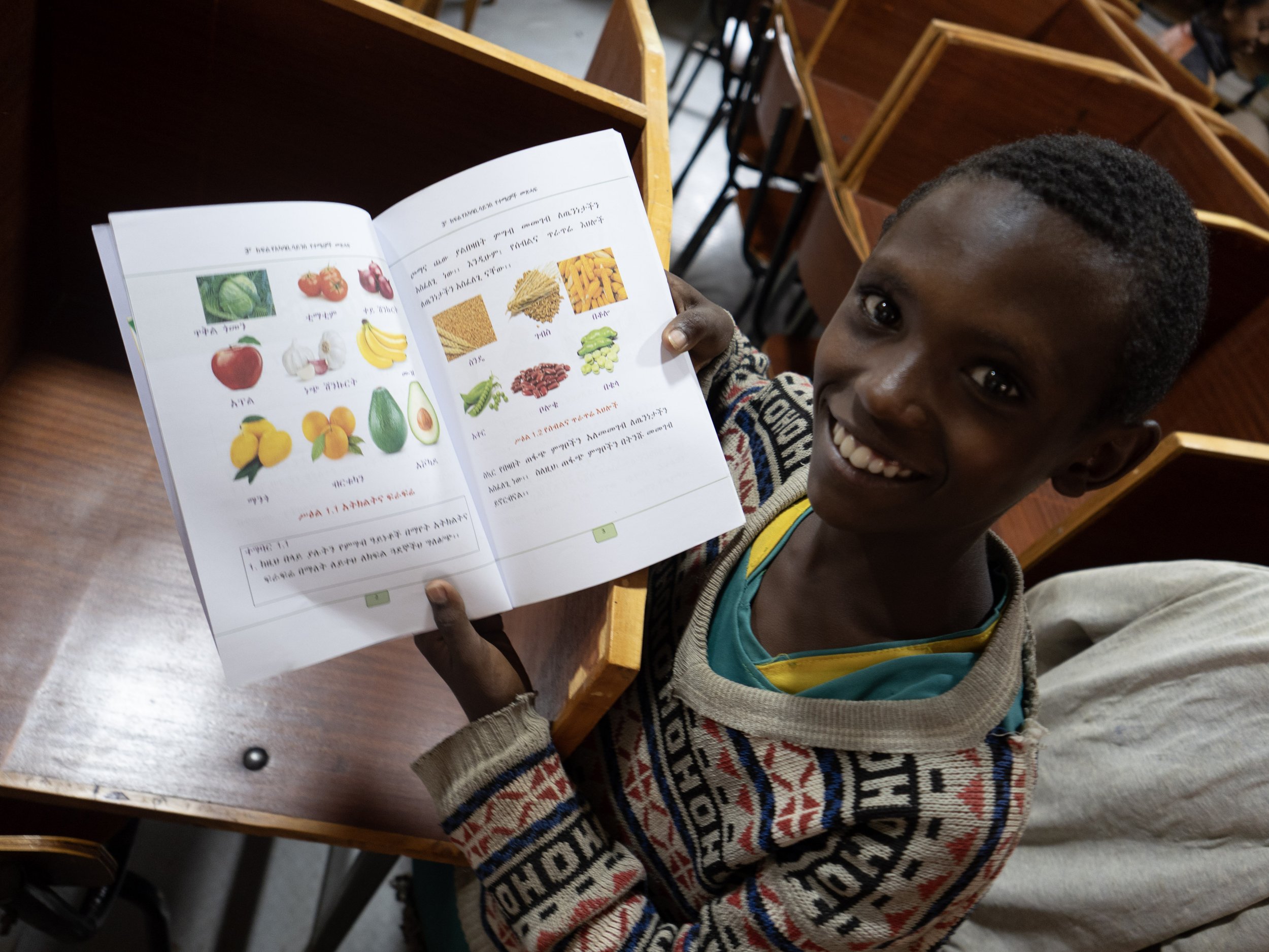 Nuori poika lukee kuvakirjaa, jossa on hedelmiä ja ruokia, luokkaopetustilassa.