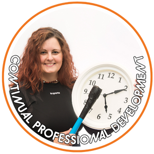 A woman with curly red hair smiling at the camera, wearing a black shirt with a lanyard. She is holding a large clock and a blue drum beater, with text around the clock reading "CONTINUOUS PROFESSIONAL DEVELOPMENT"