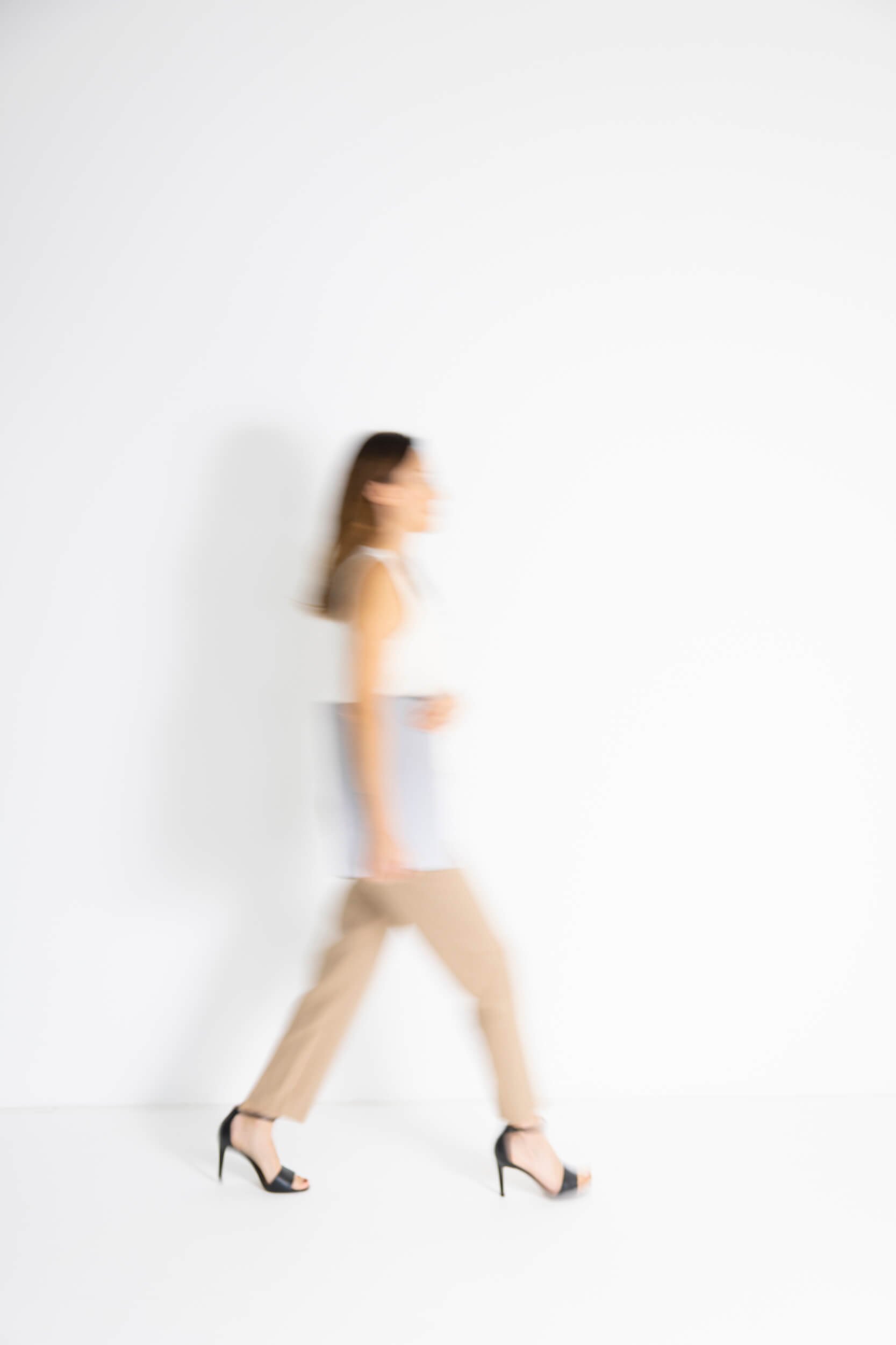 Eine Frau in hohen Schuhen läuft, die Bewegung ist unscharf, vor einem weißen Hintergrund.