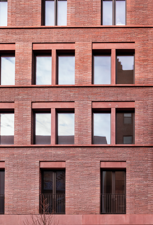 A brick apartment building with multiple windows reflecting the sky and neighboring structures.