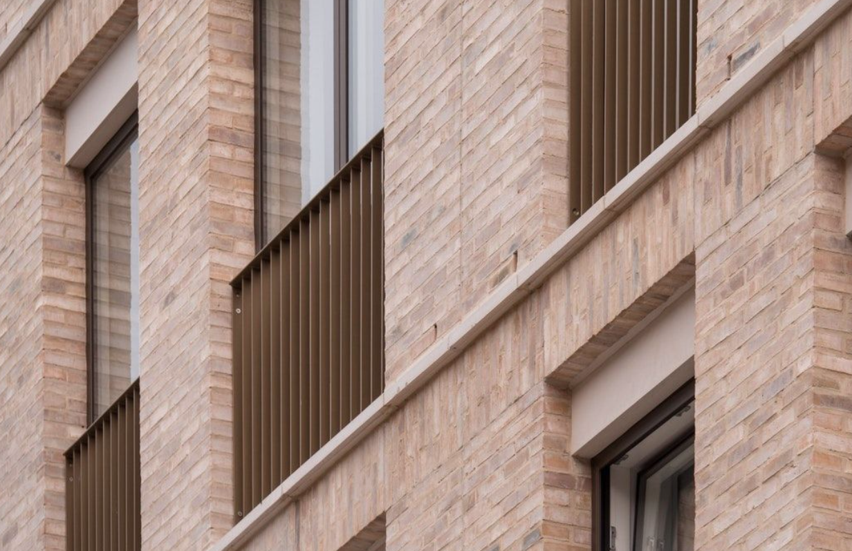 Close-up view of a corner of a brick apartment building with balconies and windows.