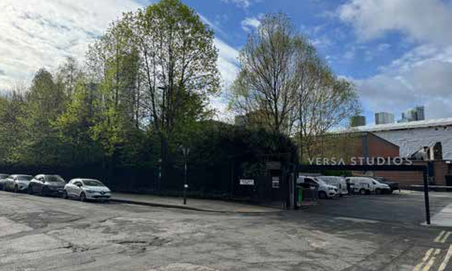 Entrance to Versus Studios with parked cars and trees in the background, partly cloudy sky.