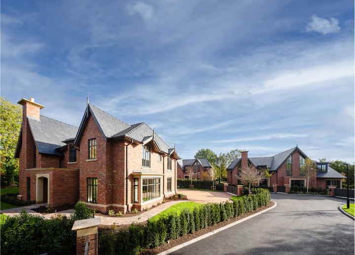 Residential neighborhood with large brick houses, well-maintained lawns, and a curved street under a partly cloudy sky.