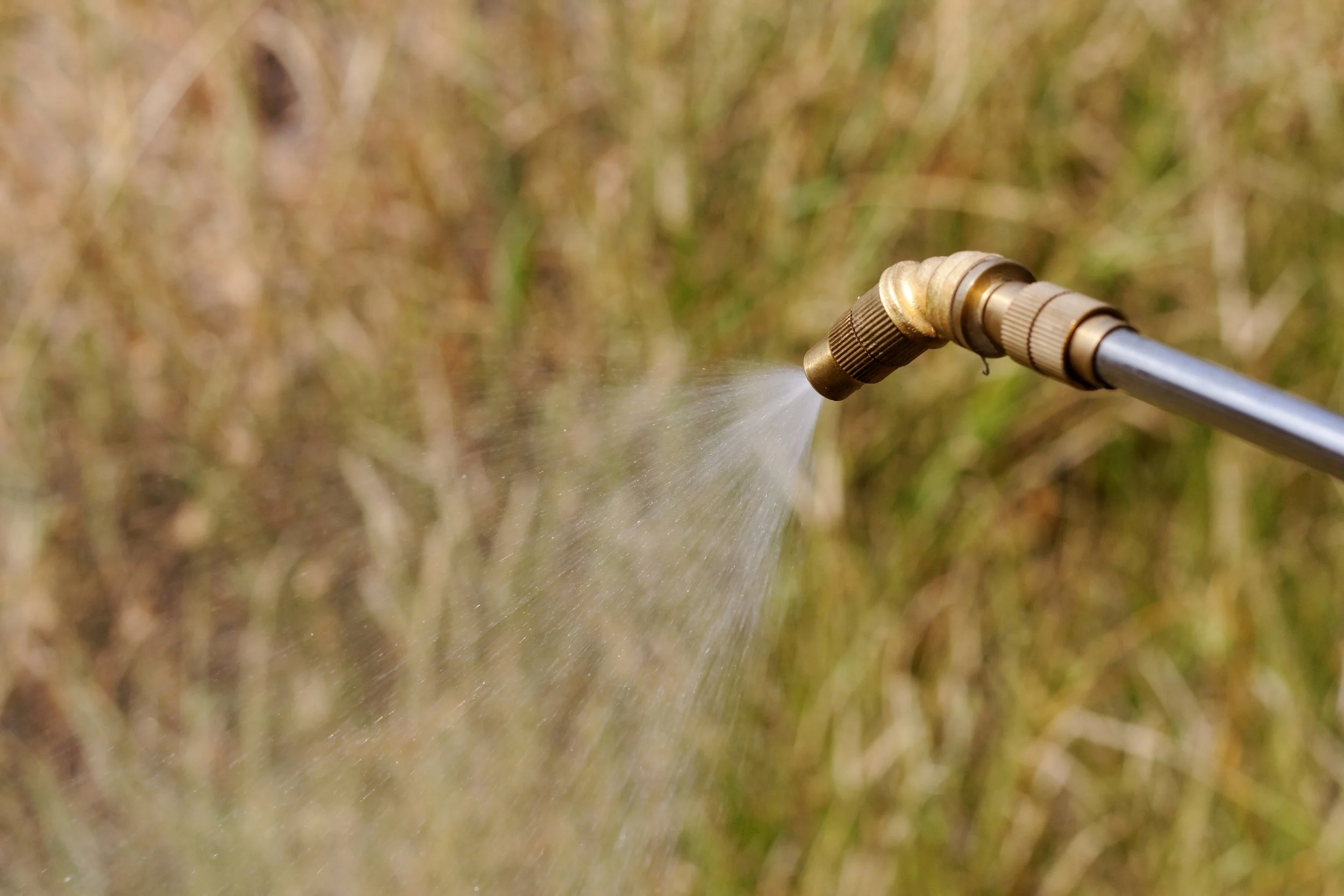 Close-up of a metal spray nozzle spraying chemical on weeds